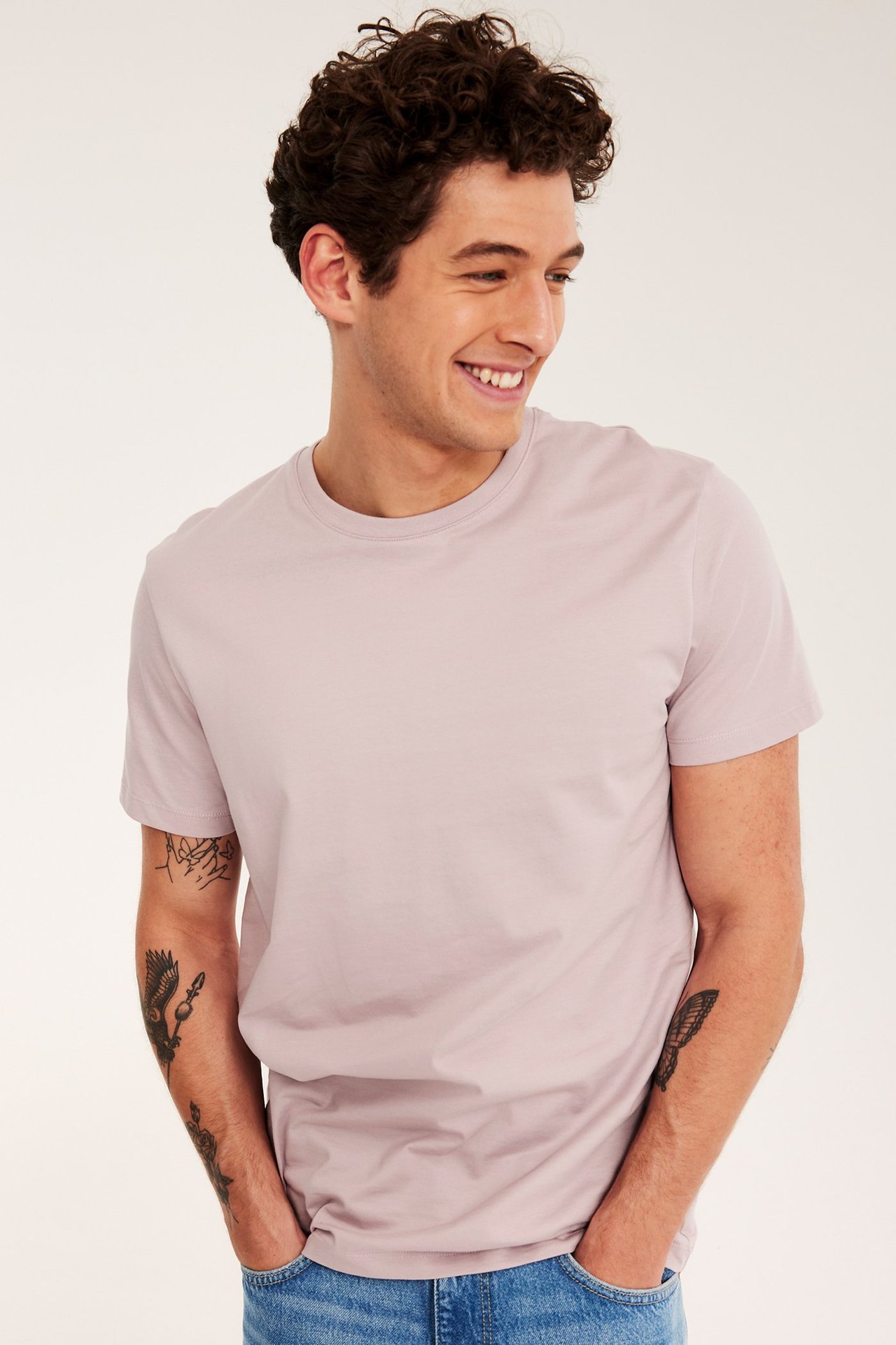 Widok z przodu mężczyzny w jasnoróżowym bawełnianym T-shircie i niebieskich dżinsach.