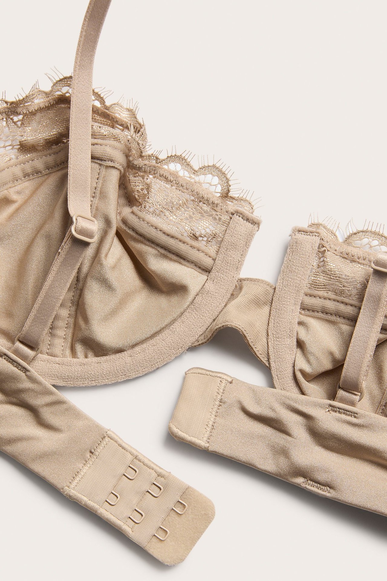 Zbliżenie na jasnobrązowy koronkowy biustonosz balconette, z regulowanymi ramiączkami i zapięciem na haftki.