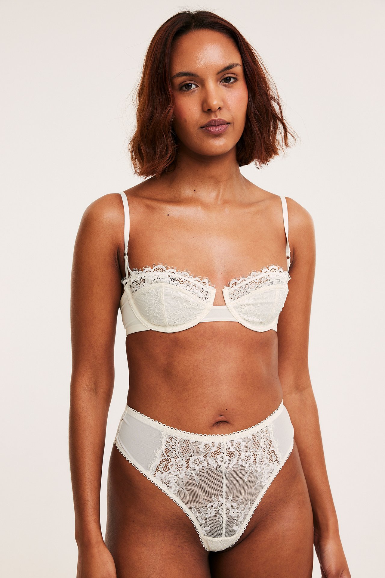 Framifrån på en kvinna i offwhite spetsbalconette-bh och matchande högmidjade trosor.