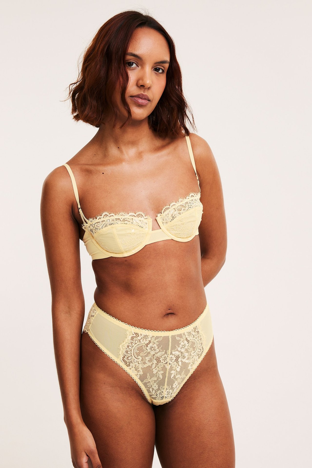Framsida av en kvinna som bär en ljusgul spetsbalconette-bh med matchande spetstrosor.