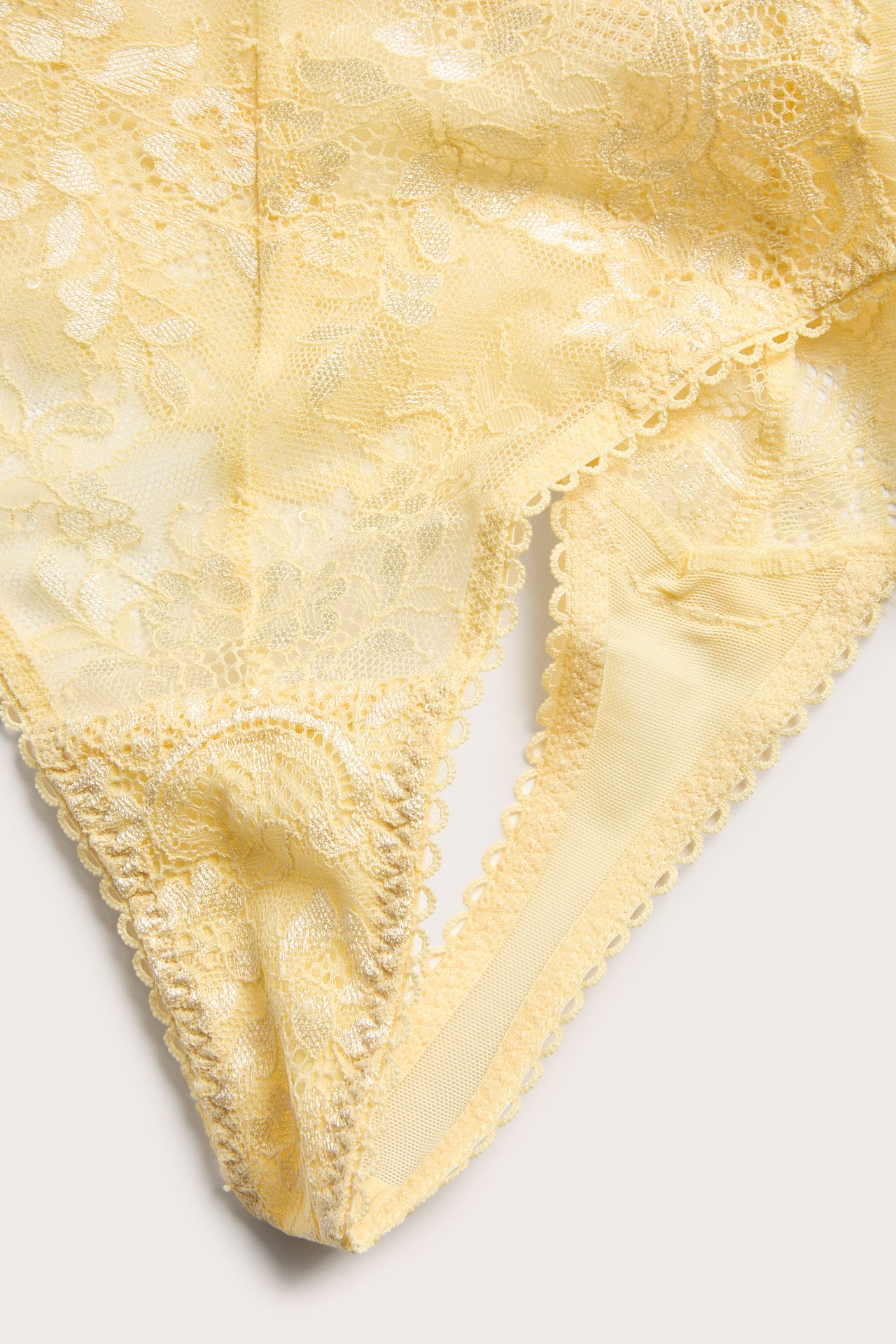 Zbliżenie jasnożółtych koronkowych stringów z delikatnymi kwiatowymi detalami.