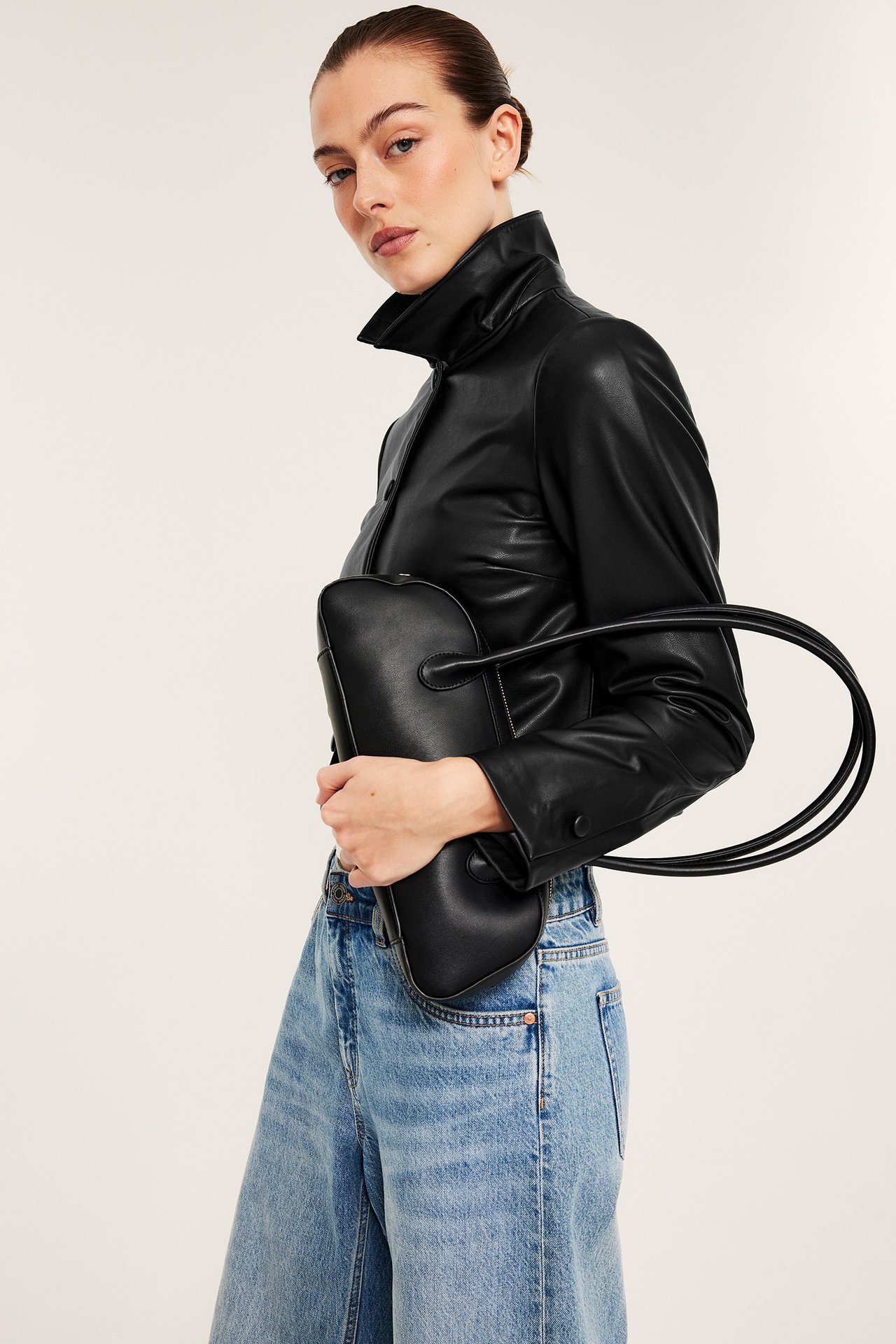 Edestäpäin: nainen pitää mustaa bowlinglaukkua, yllään musta nahkapaita ja vaaleansiniset farkut.