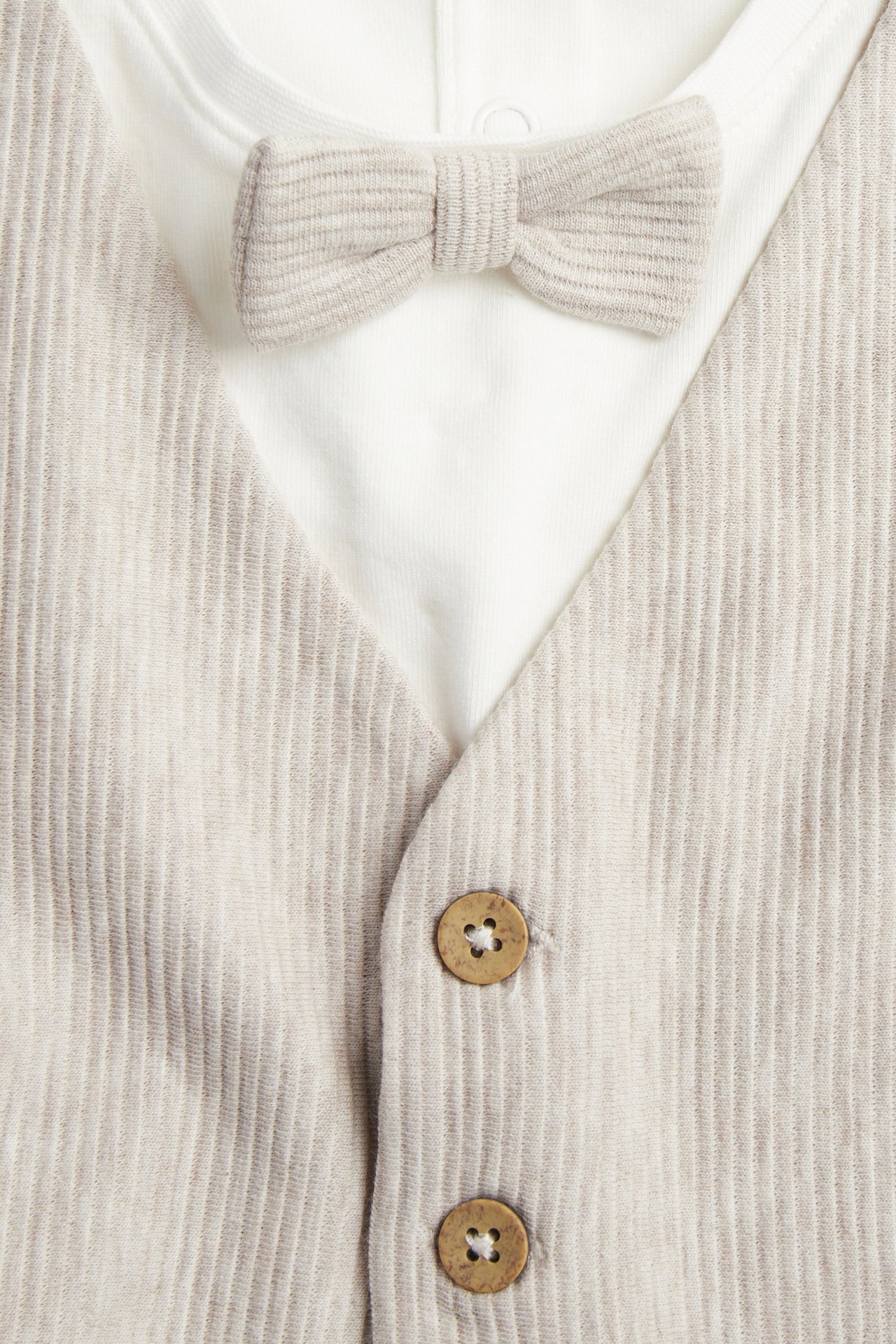 Zbliżenie: Beżowe, melanżowe body niemowlęce z doszytą kamizelką, ozdobnymi guzikami i muchą.