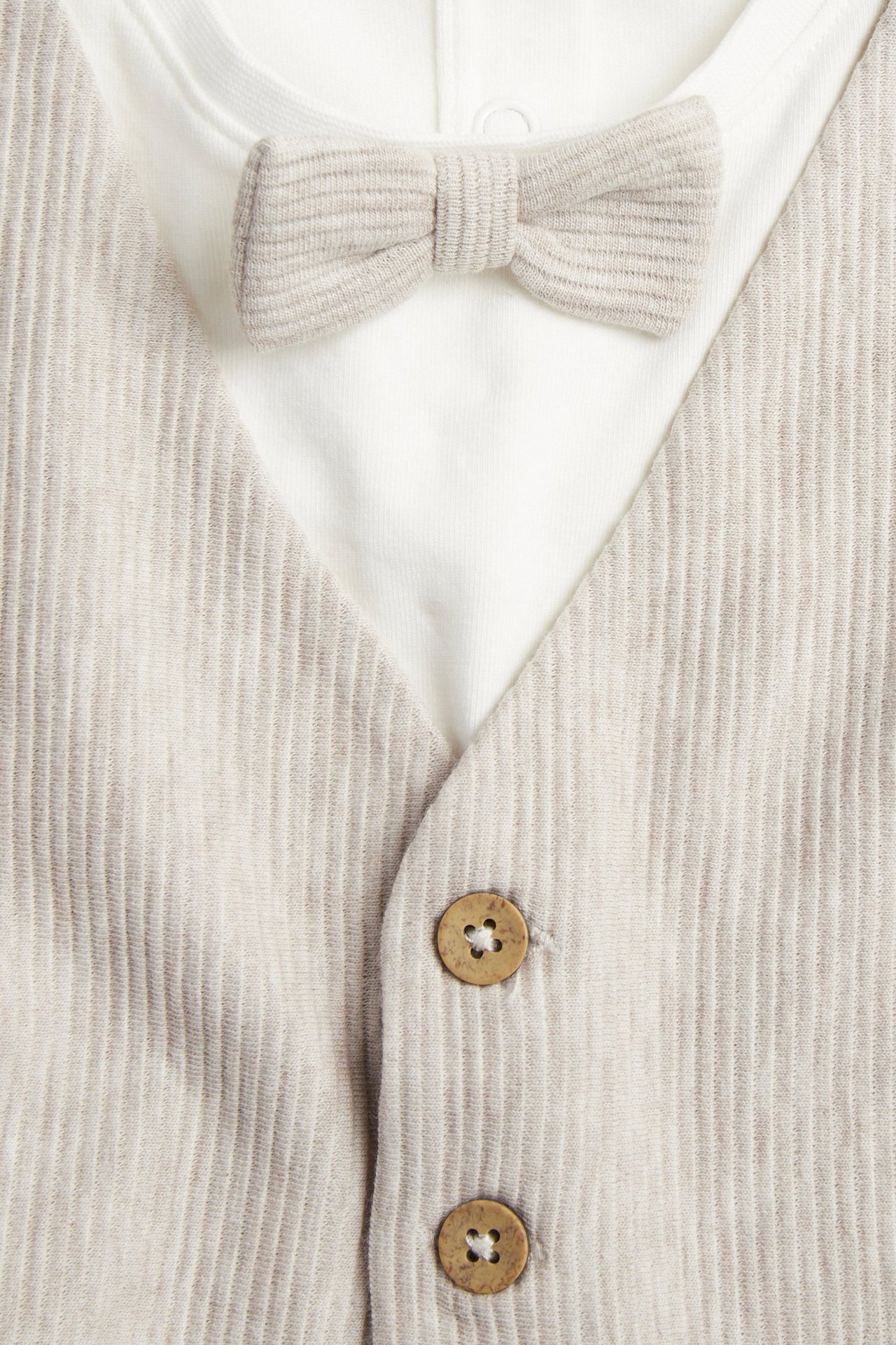 Zbliżenie: Beżowe, melanżowe body niemowlęce z doszytą kamizelką, ozdobnymi guzikami i muchą.