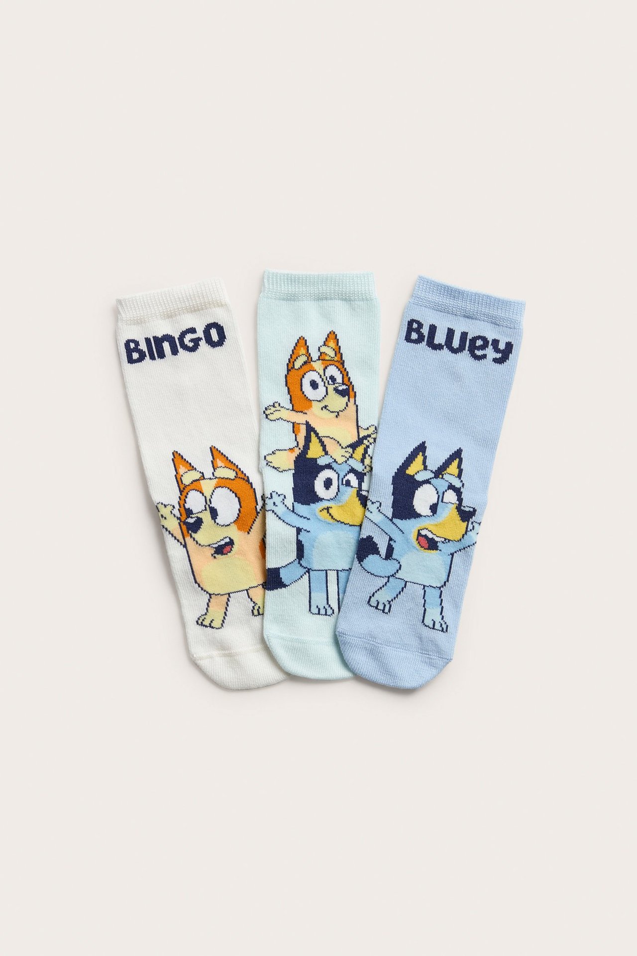 Framsida av tre barnstrumpor i bomullsmix: offwhite, ljusblå och blekblå, alla med Bluey-tryck.