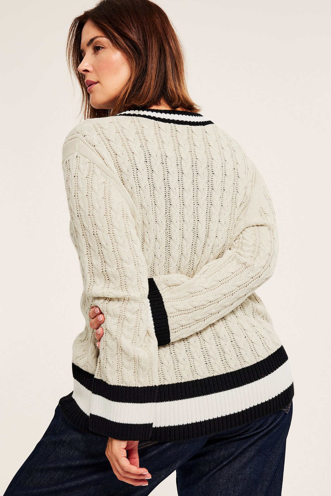Bakfra, kvinne i offwhite kabelstrikket bomullscardigan med svart-hvite striper, over mørkblå jeans.