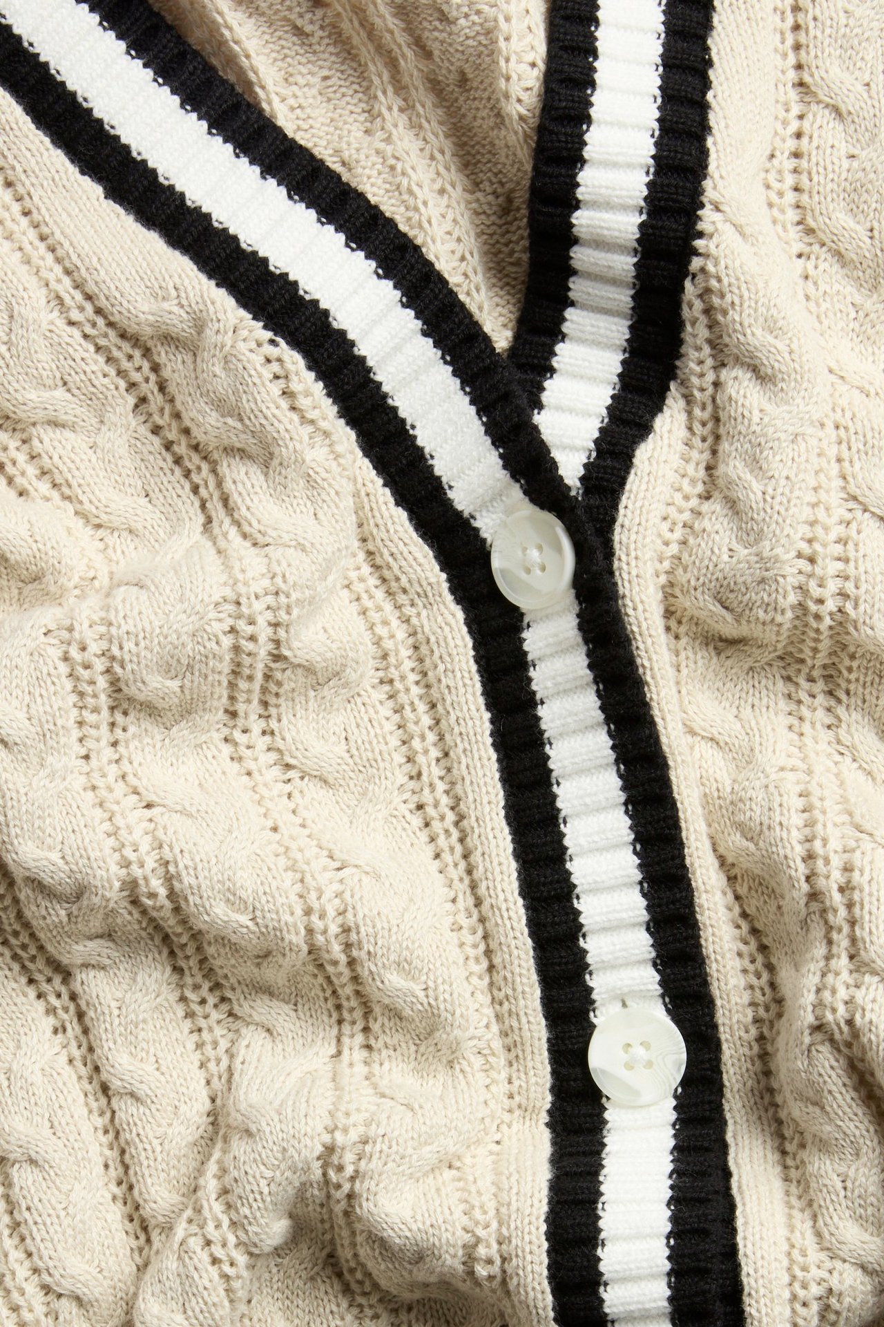 Zbliżenie: ecru, warkoczowy kardigan bawełniany, dekolt w serek w paski, białe guziki.