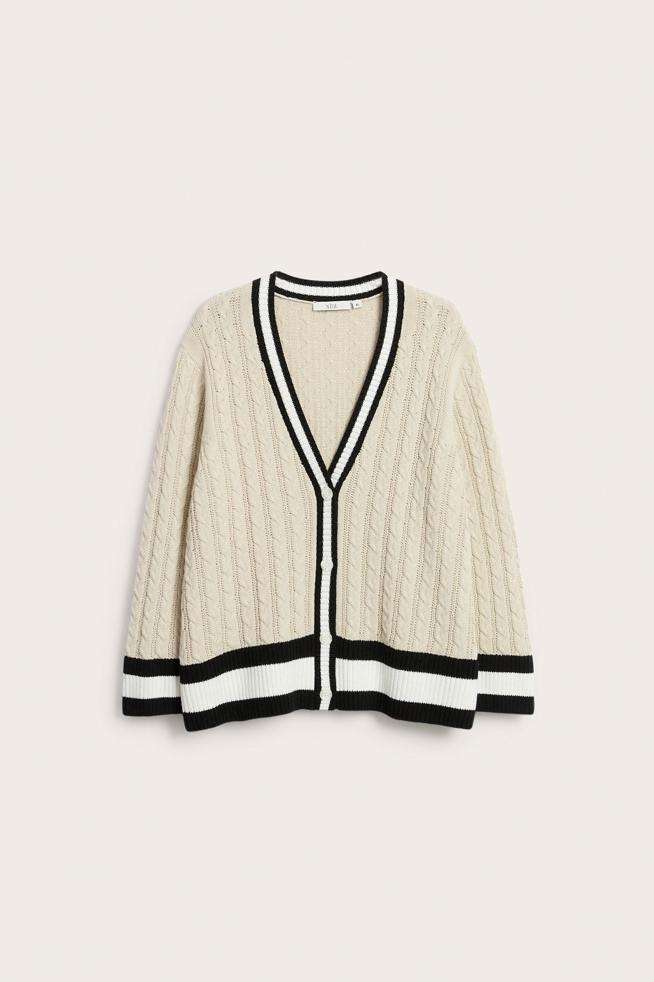Frontvisning av en offwhite kabelstrikket bomullscardigan med V-hals, svart-hvit stripet kant og knapper foran.