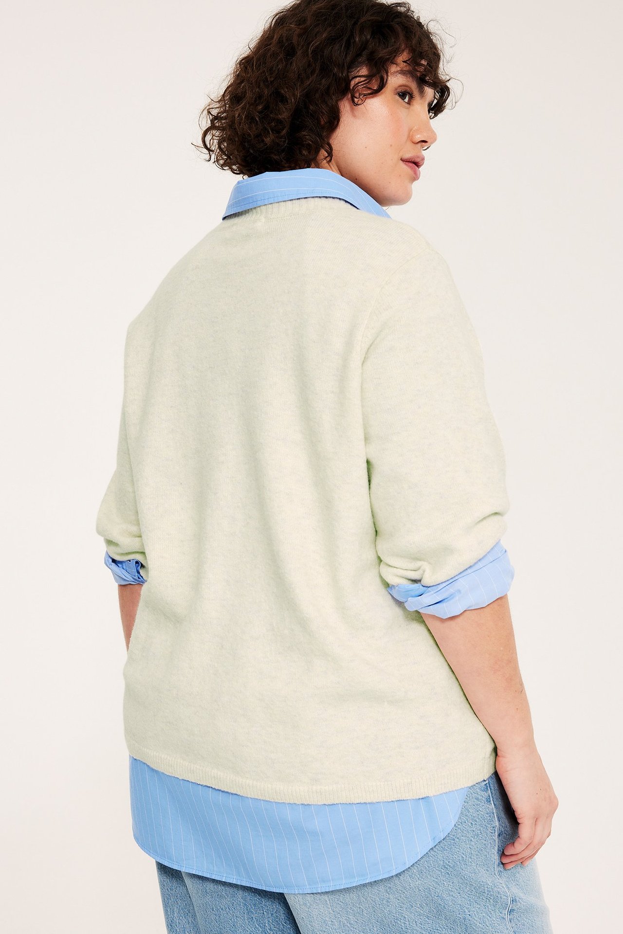 Nainen päällään luonnonvalkoinen meleerattu neulottu 3/4-hihainen toppi, alla siniraitainen paita.