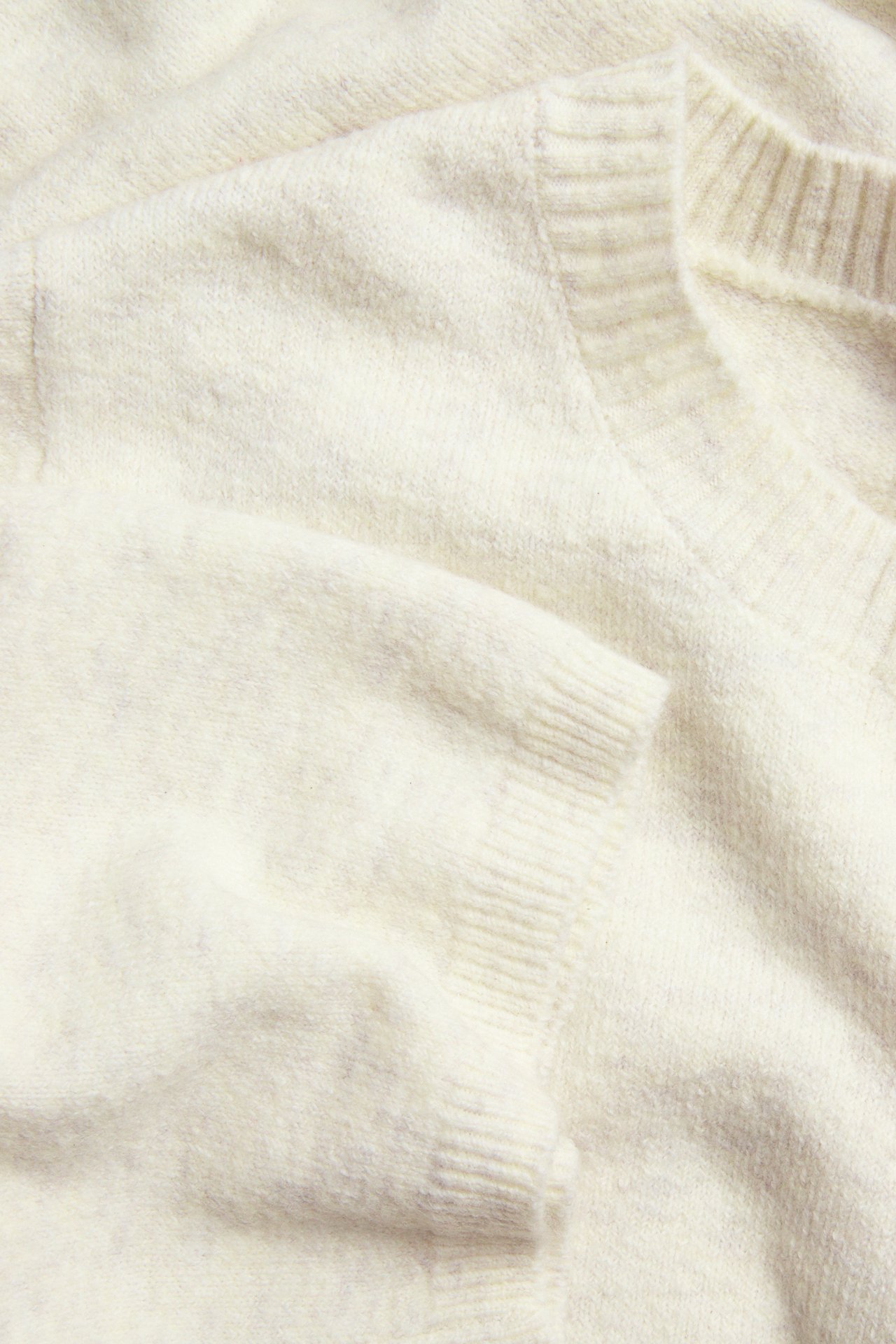 Lähikuva taitetusta luonnonvalkoisesta meleeratusta neule-t-paidasta, jossa on pyöreä pääntie ja 3/4-hihat.