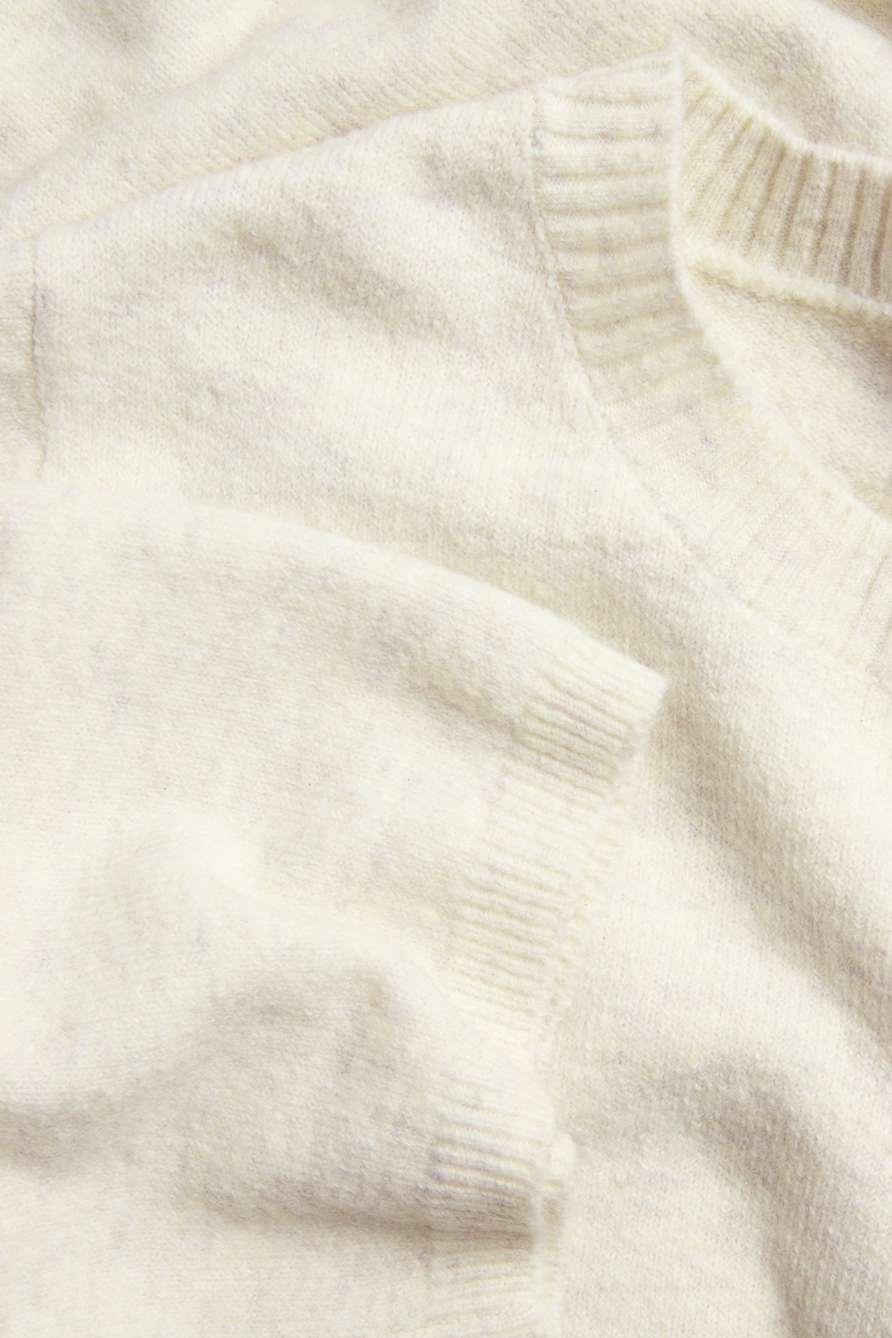 Zbliżenie złożonej dzianinowej koszulki w kolorze złamanej bieli, melanżowej, z okrągłym dekoltem i rękawami 3/4.