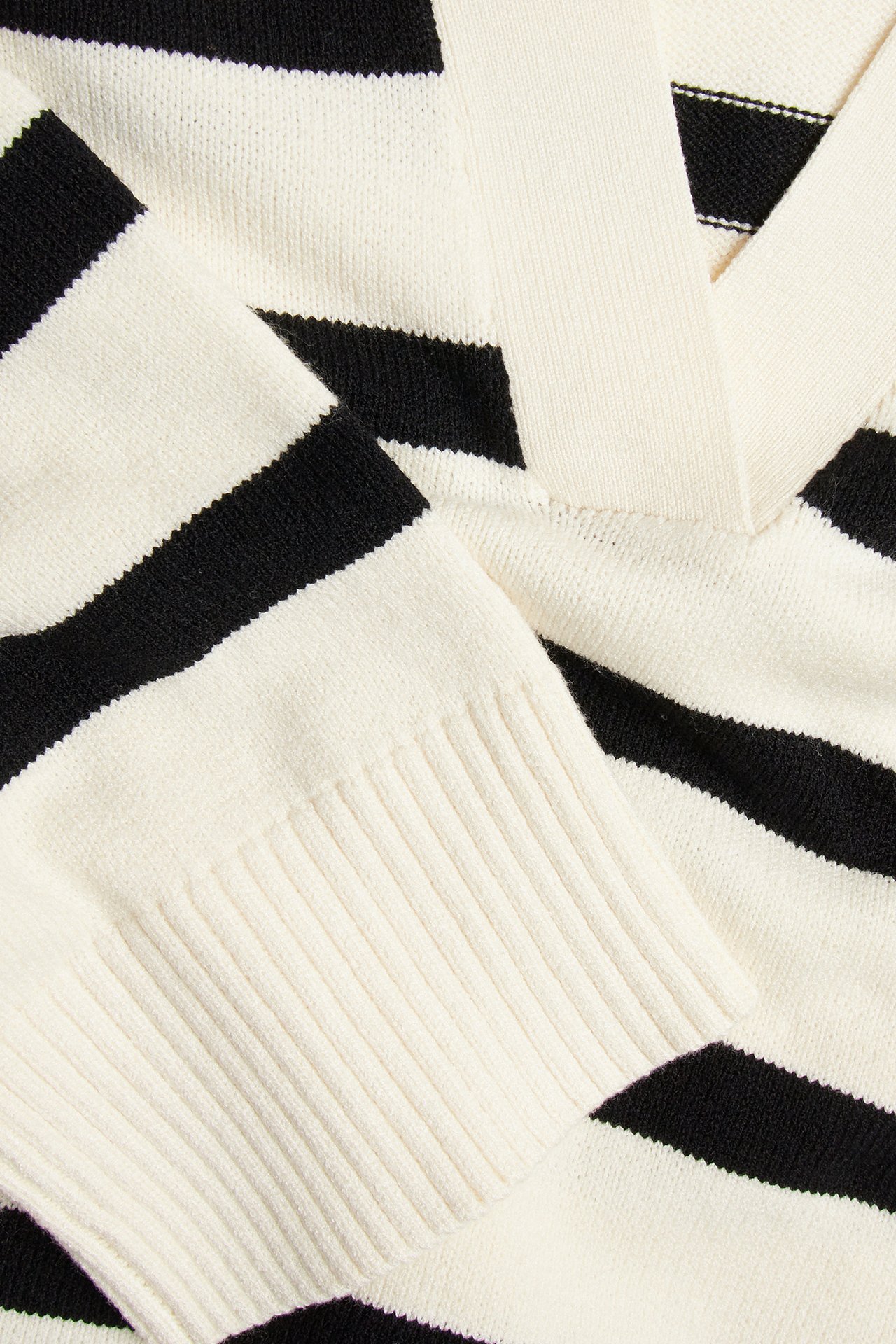 Nærbilde av en offwhite-svartstripet strikkegenser med v-hals krage og ribbemansjetter.