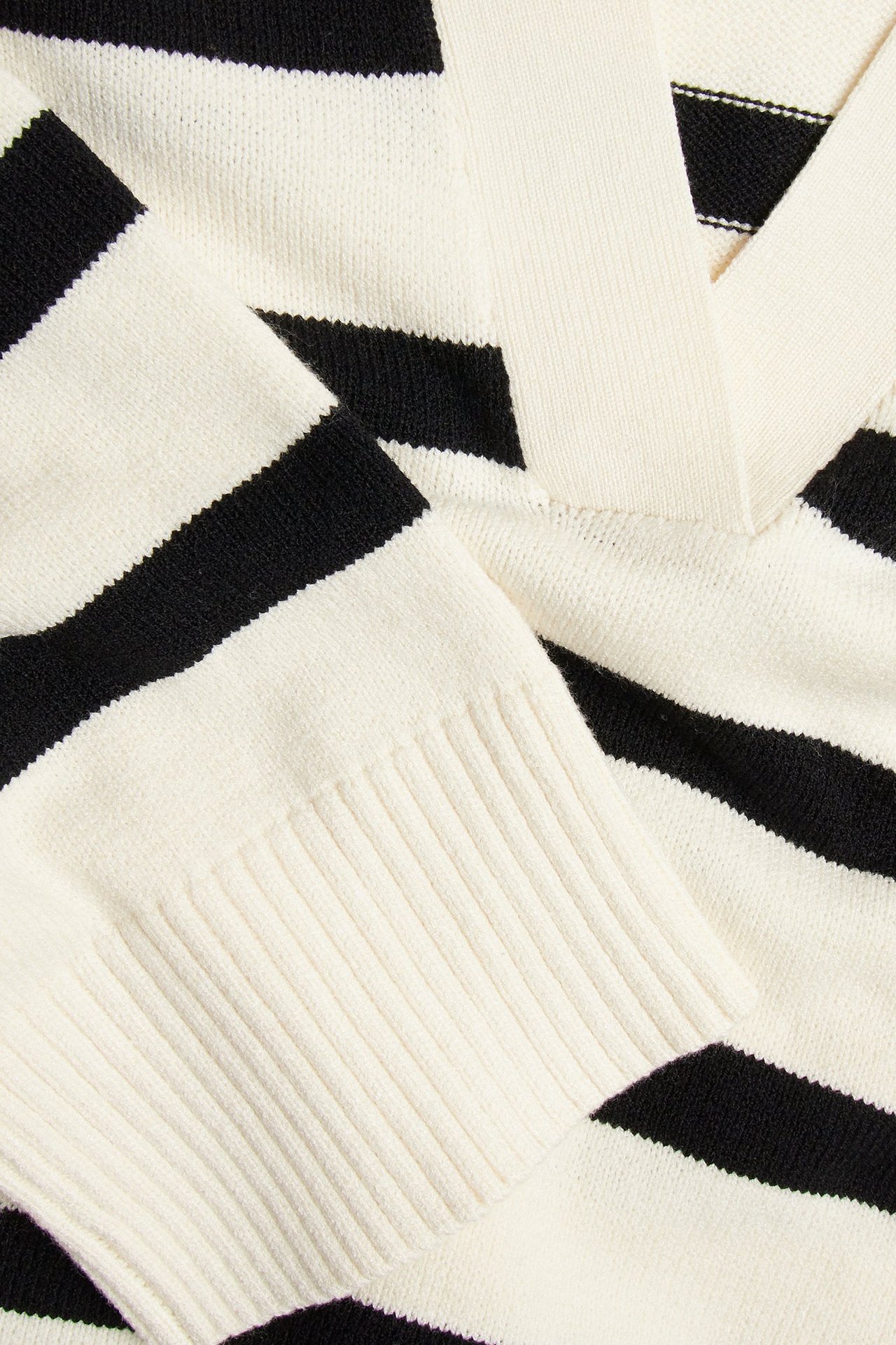 Zbliżenie na sweter w paski off-white i czarne, z kołnierzem w serek i ściągaczami.