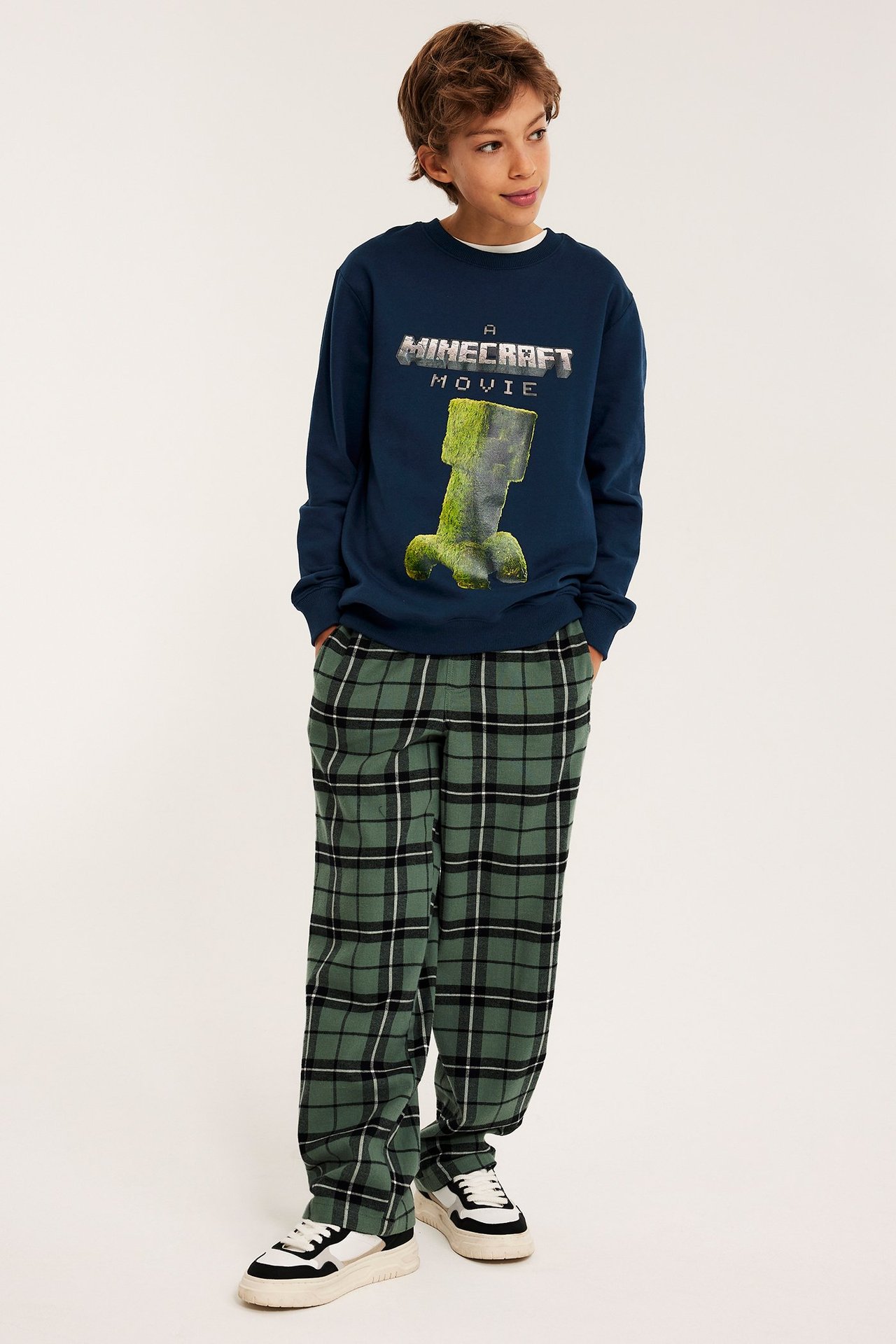 Forfra: barn i mørkeblå Minecraft Creeper-genser, grønne rutete bukser og hvite joggesko.
