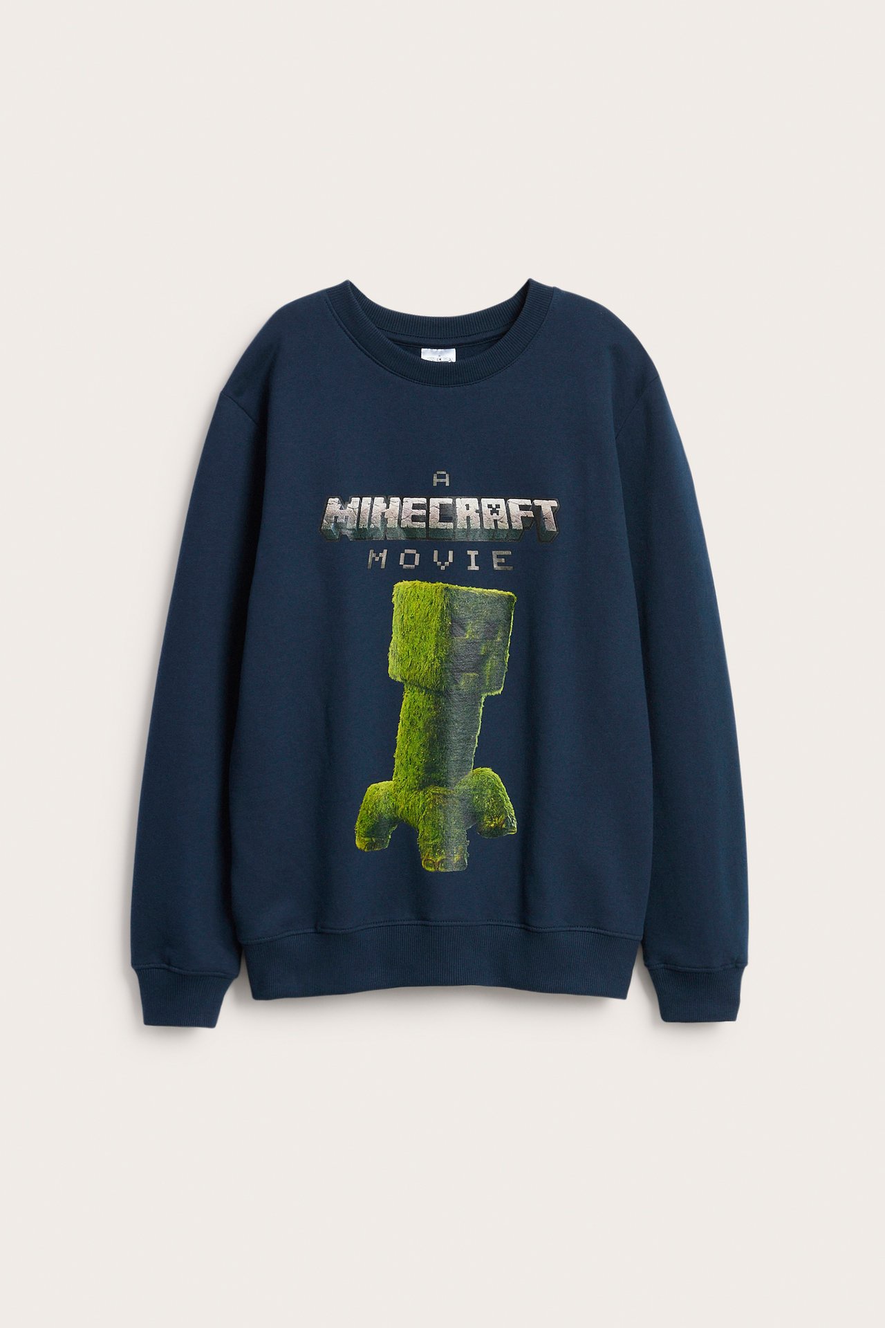 Frontbilde av en mørkeblå bomullssweatshirt for barn med "Minecraft Movie"-tekst og grønt Creeper-trykk.