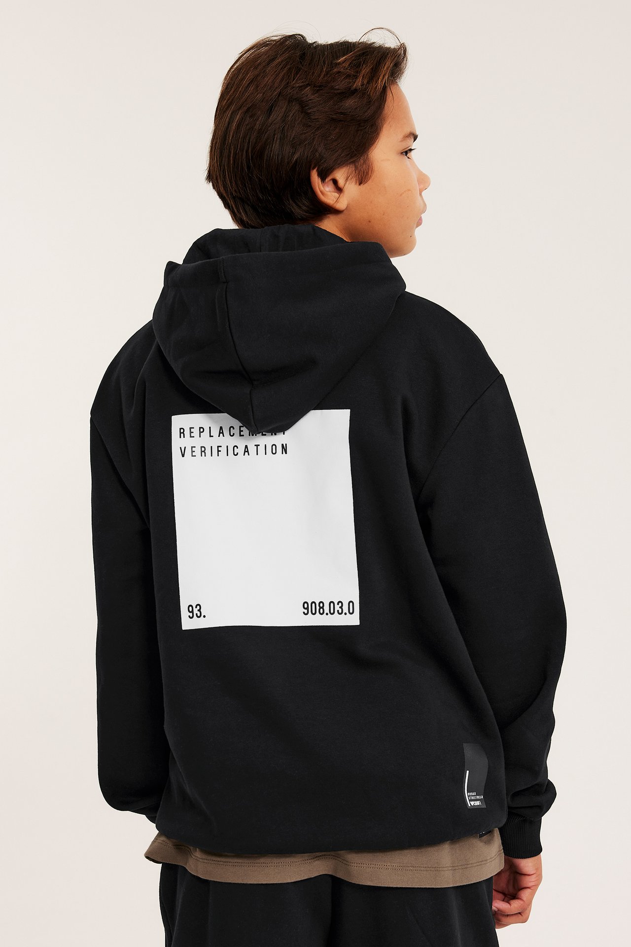 Tyłem: dziecko w czarnej bluzie z kapturem z białym nadrukiem, na brązowej koszulce.