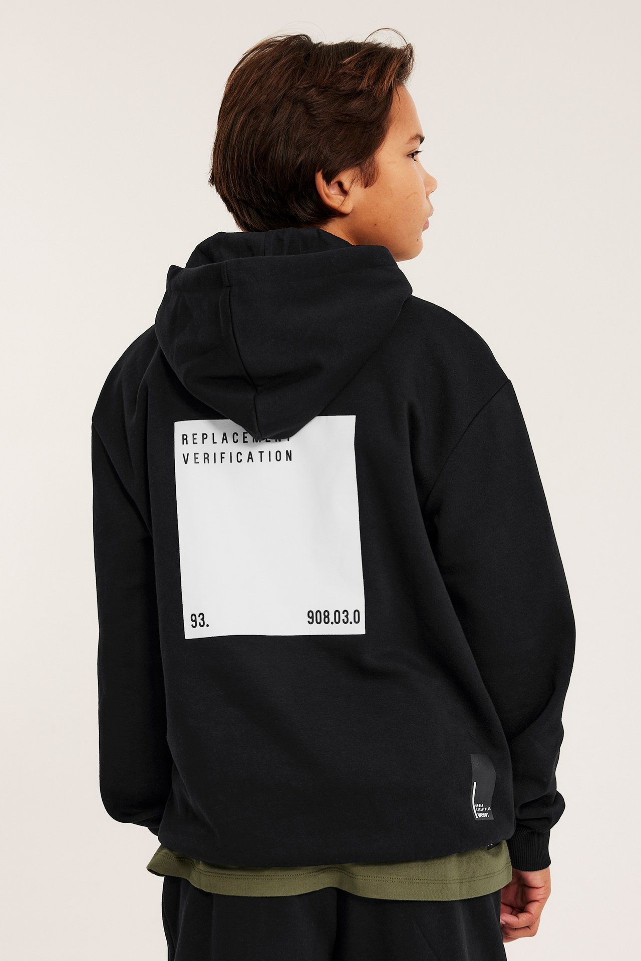 Ryggvy av ett barn i svart hoodie med vitt grafiskt tryck, buren över en grön t-shirt.