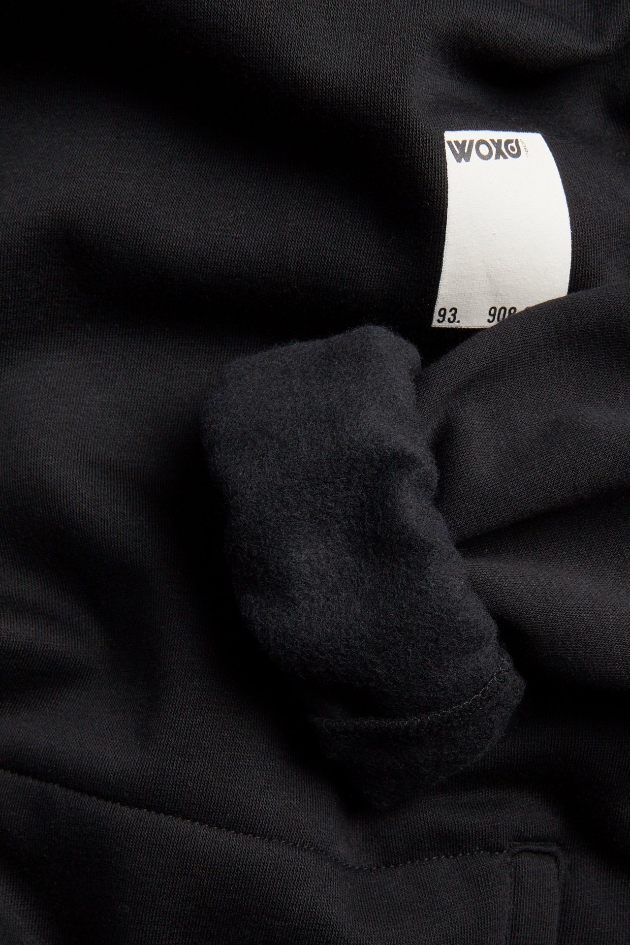 Zbliżenie czarnej tkaniny bluzy, ukazujące miękki wewnętrzny polar i białą metkę WOXG.