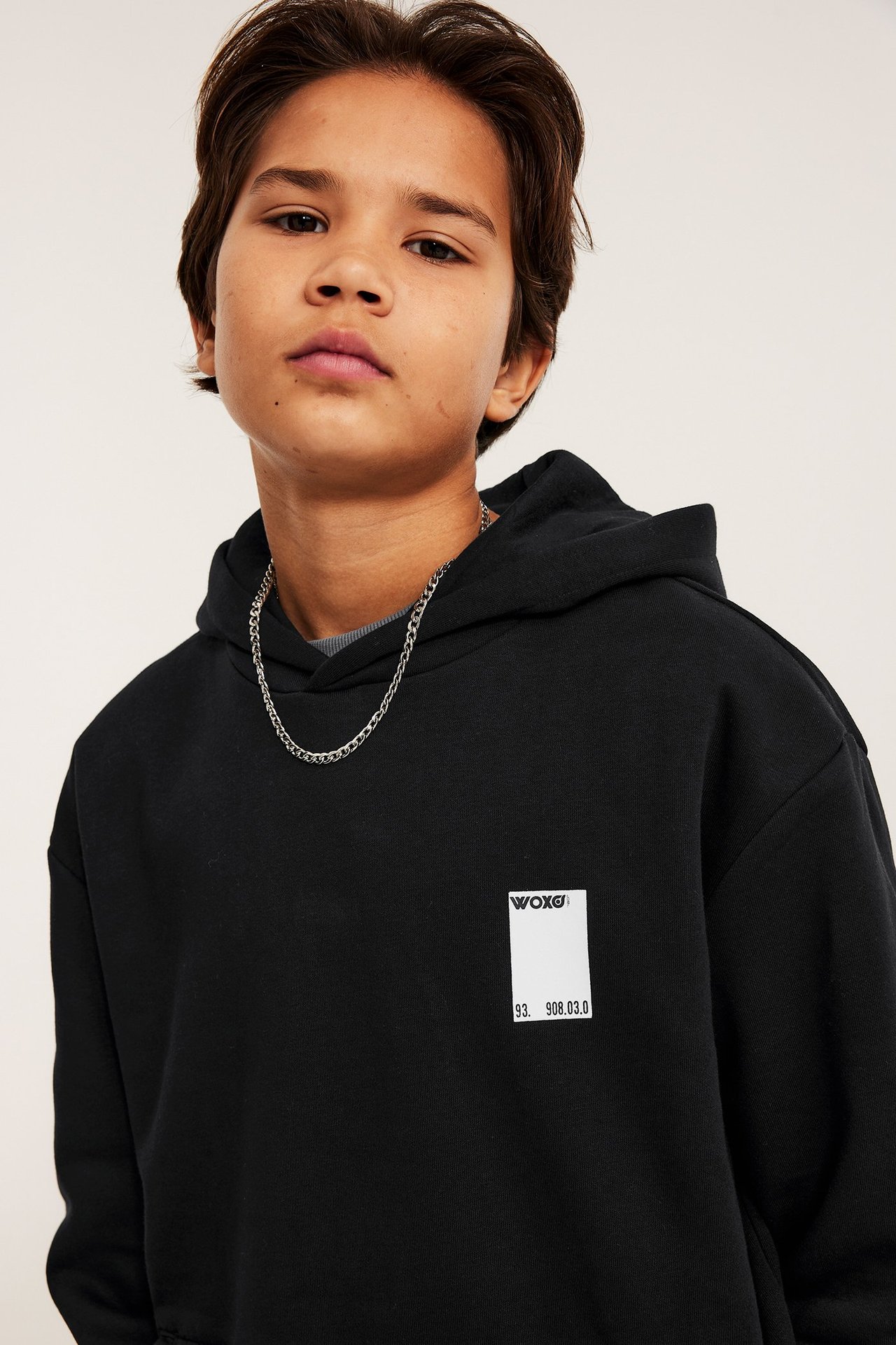 Widok z przodu: dziecko w czarnej bluzie z białym nadrukiem na piersi i srebrnym łańcuszkiem.