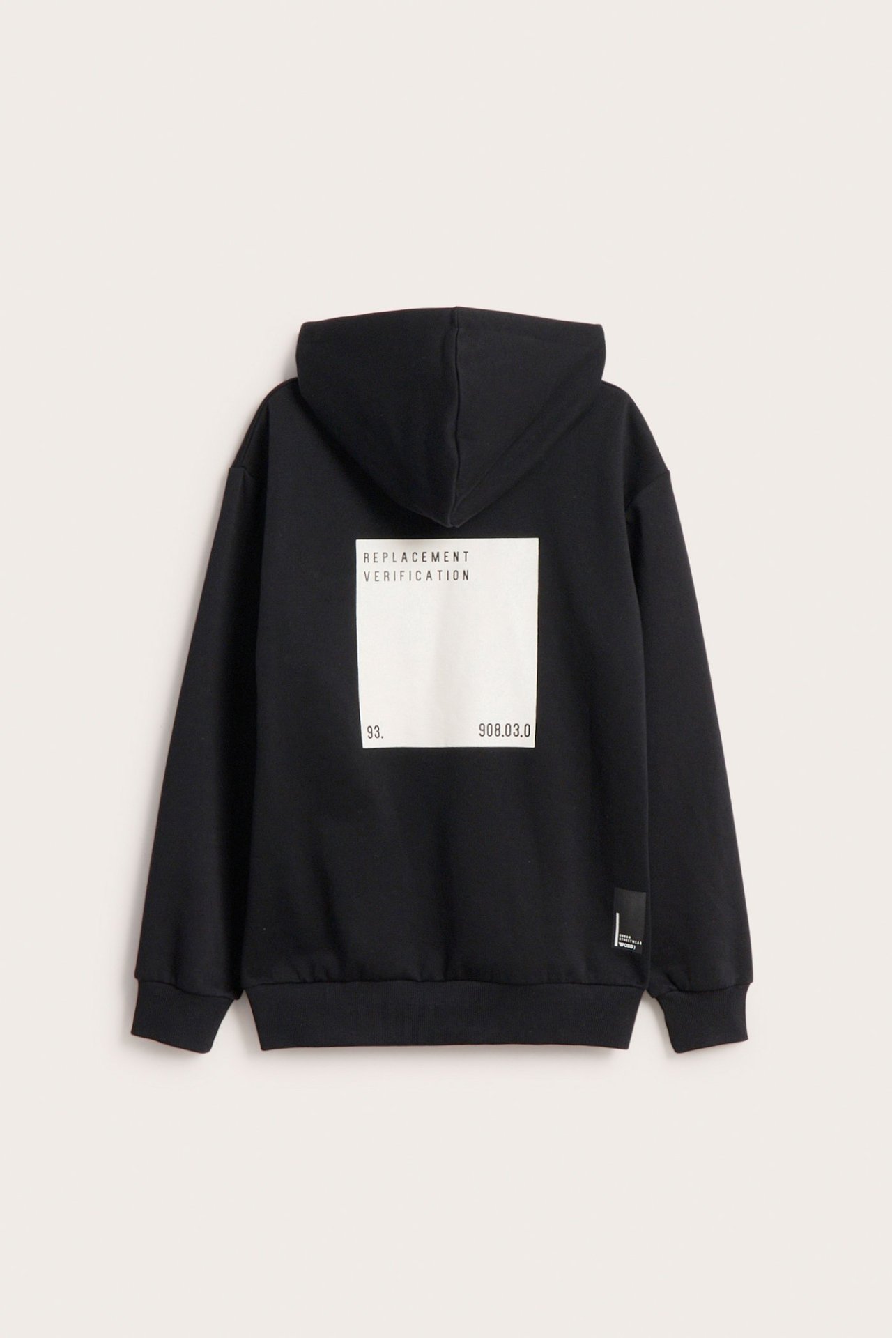 Widok z tyłu czarnej, luźnej bluzy z kapturem z białym prostokątnym gumowym nadrukiem na plecach.