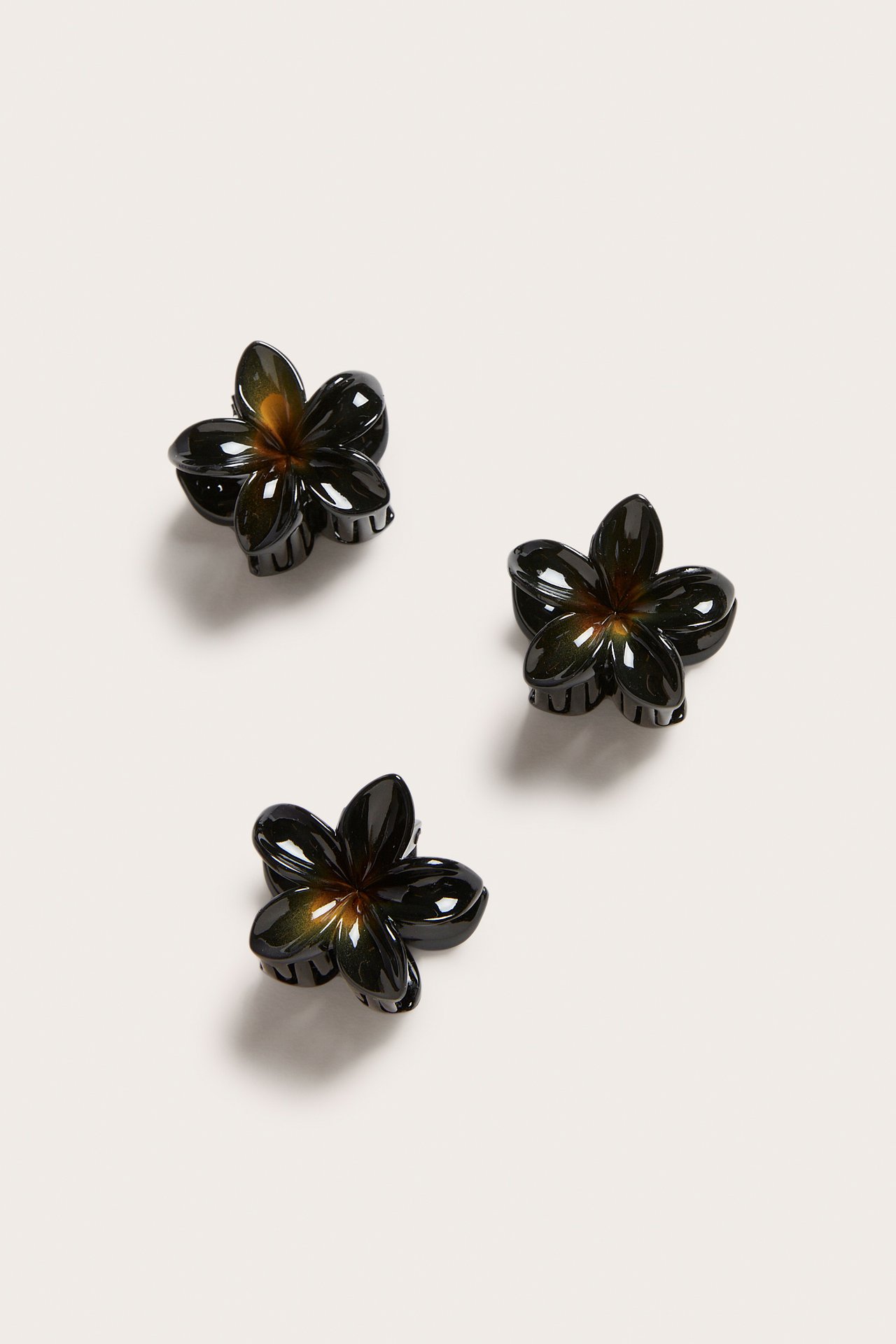 Närbild av tre små svarta blomformade hårklämmor med en diskret brun mitt.