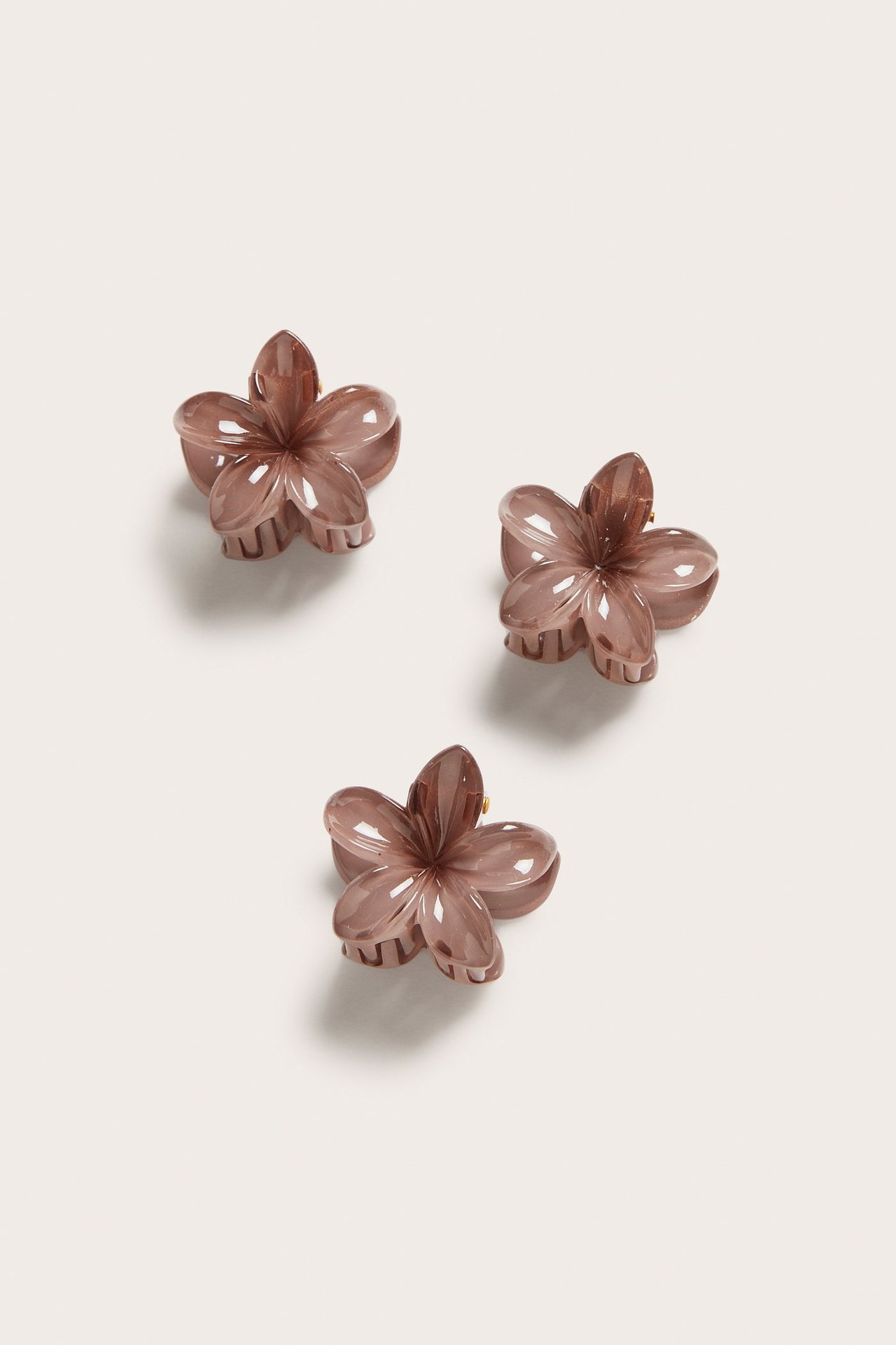 Framifrån, tre små, genomskinliga rosa blomformade hårklämmor i ett 3-pack.