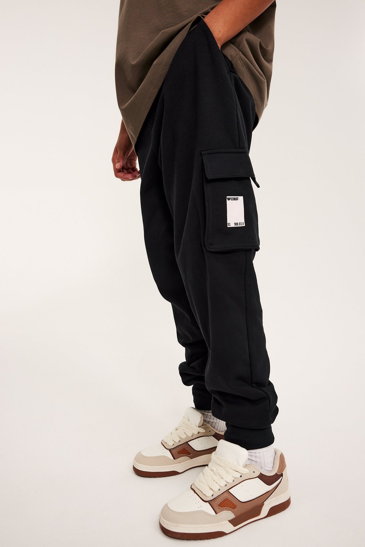 Mustat collegehousut rahtitaskuilla ja valkoisella painatuksella, ruskea t-paita sekä beiget tennarit.