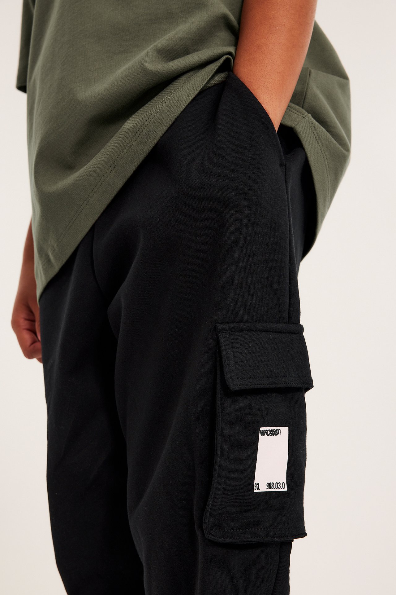 Närbild på barn i svarta mjukisbyxor med vit gummitryck på cargofickan, med en grön t-shirt.