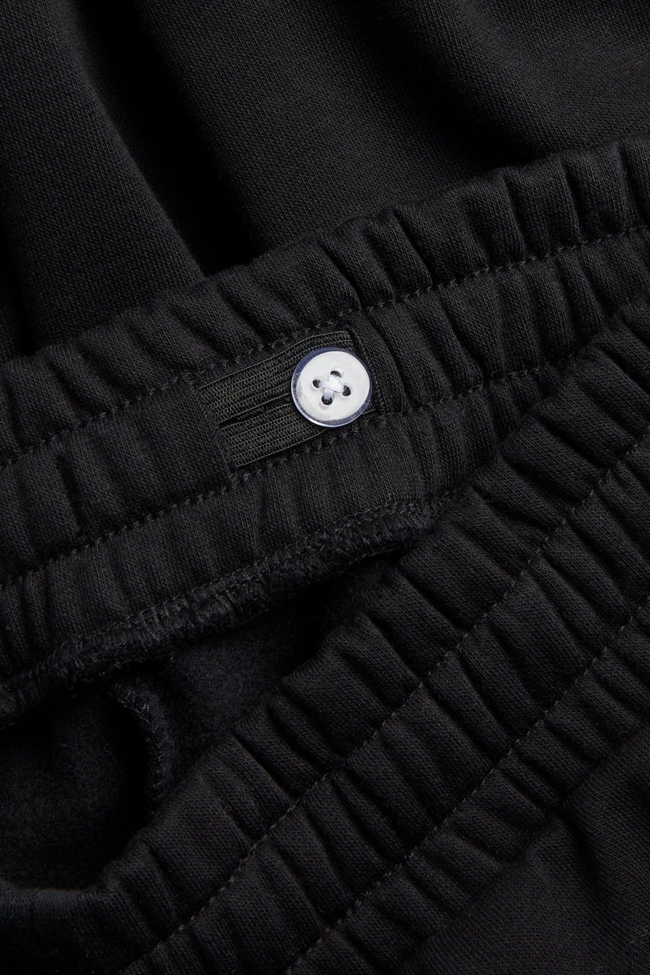 Zbliżenie czarnych spodni dresowych z elastycznym pasem i regulowanym białym guzikiem.