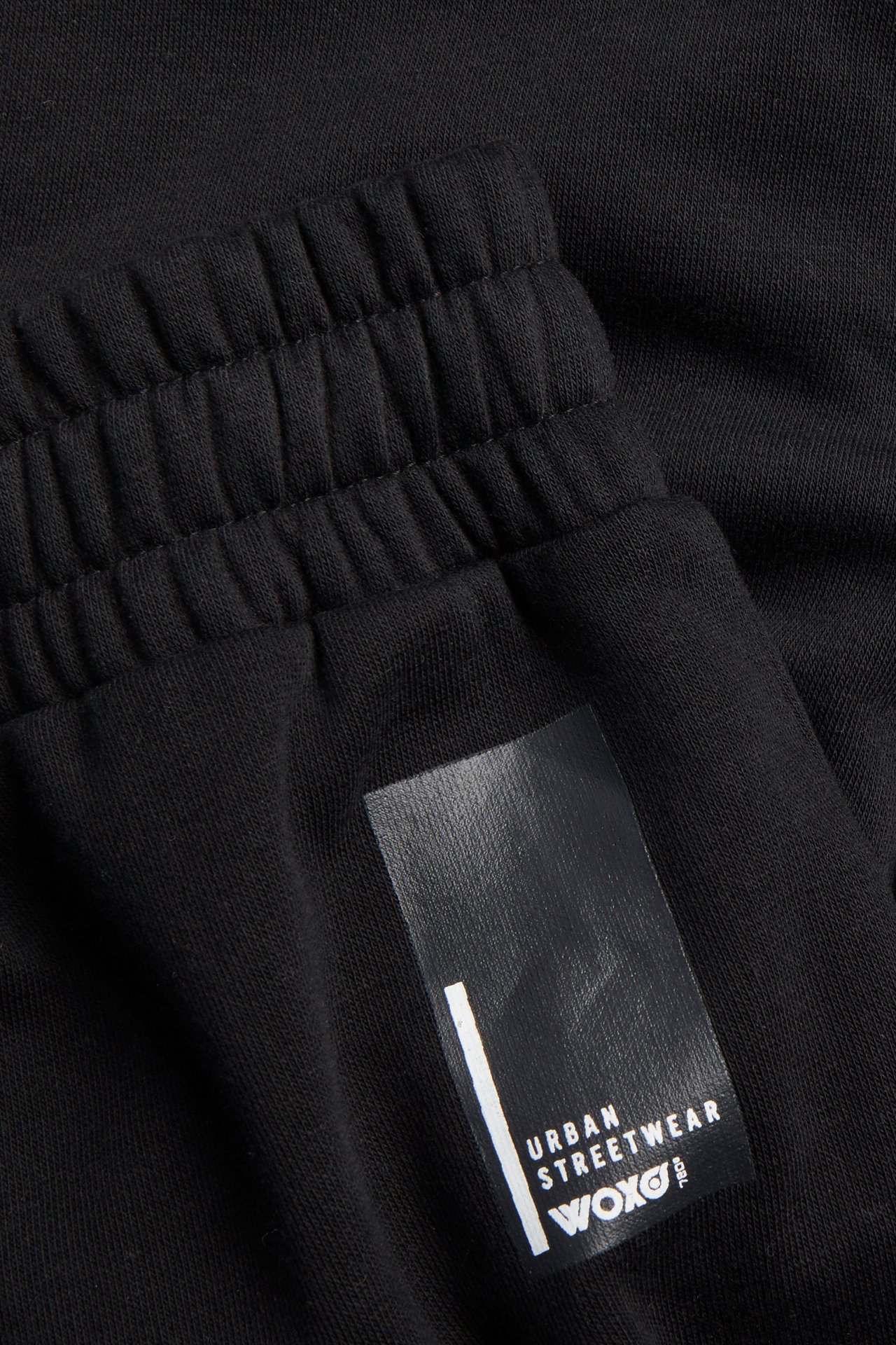 Närbild av svarta mjukisbyxor med resår i midjan och "URBAN STREETWEAR WOXO" gummitryck.
