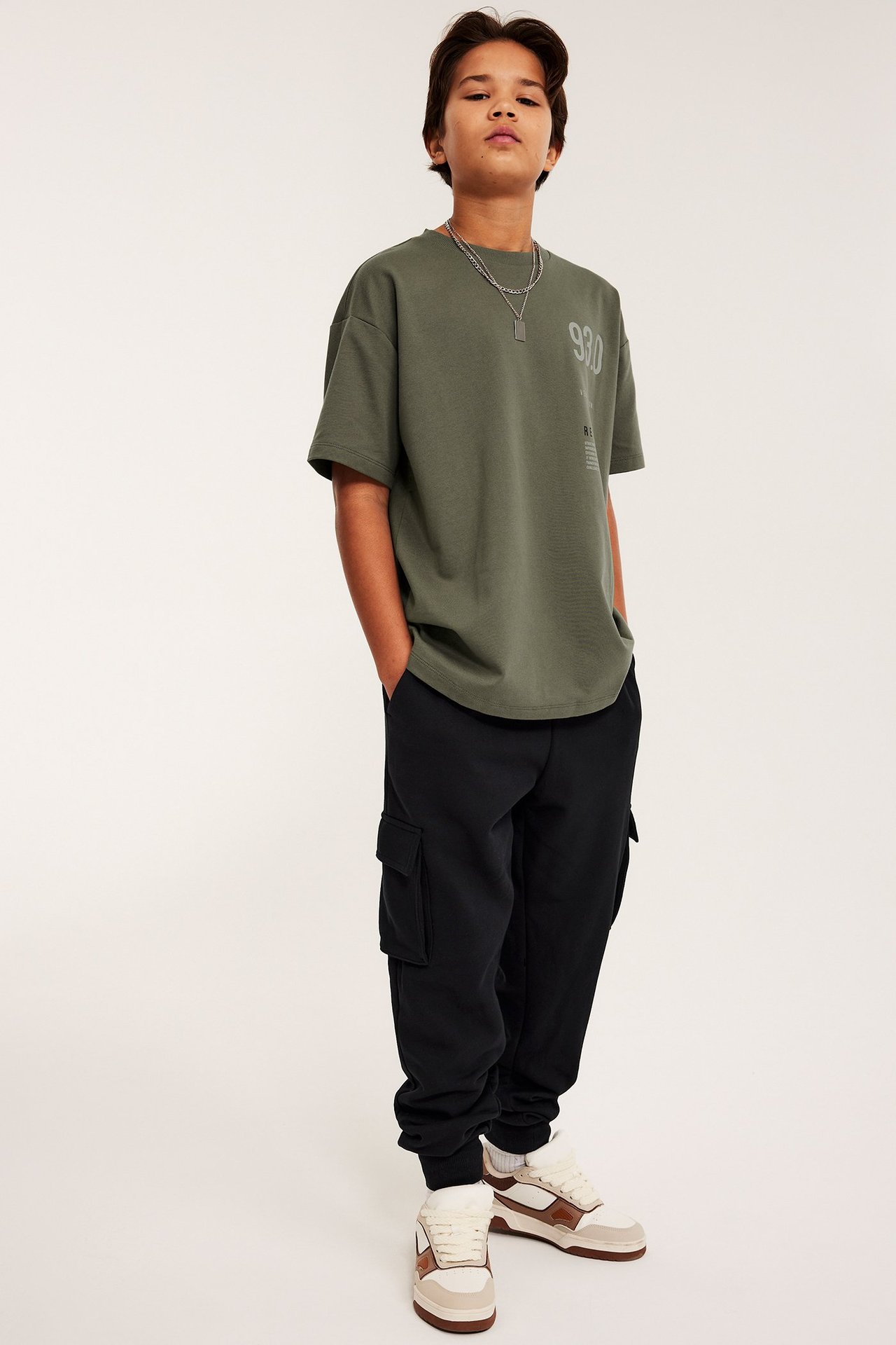 Edestä: Poika mustissa cargolenkkihousuissa, oliivinvihreässä t-paidassa ja lenkkikengissä.