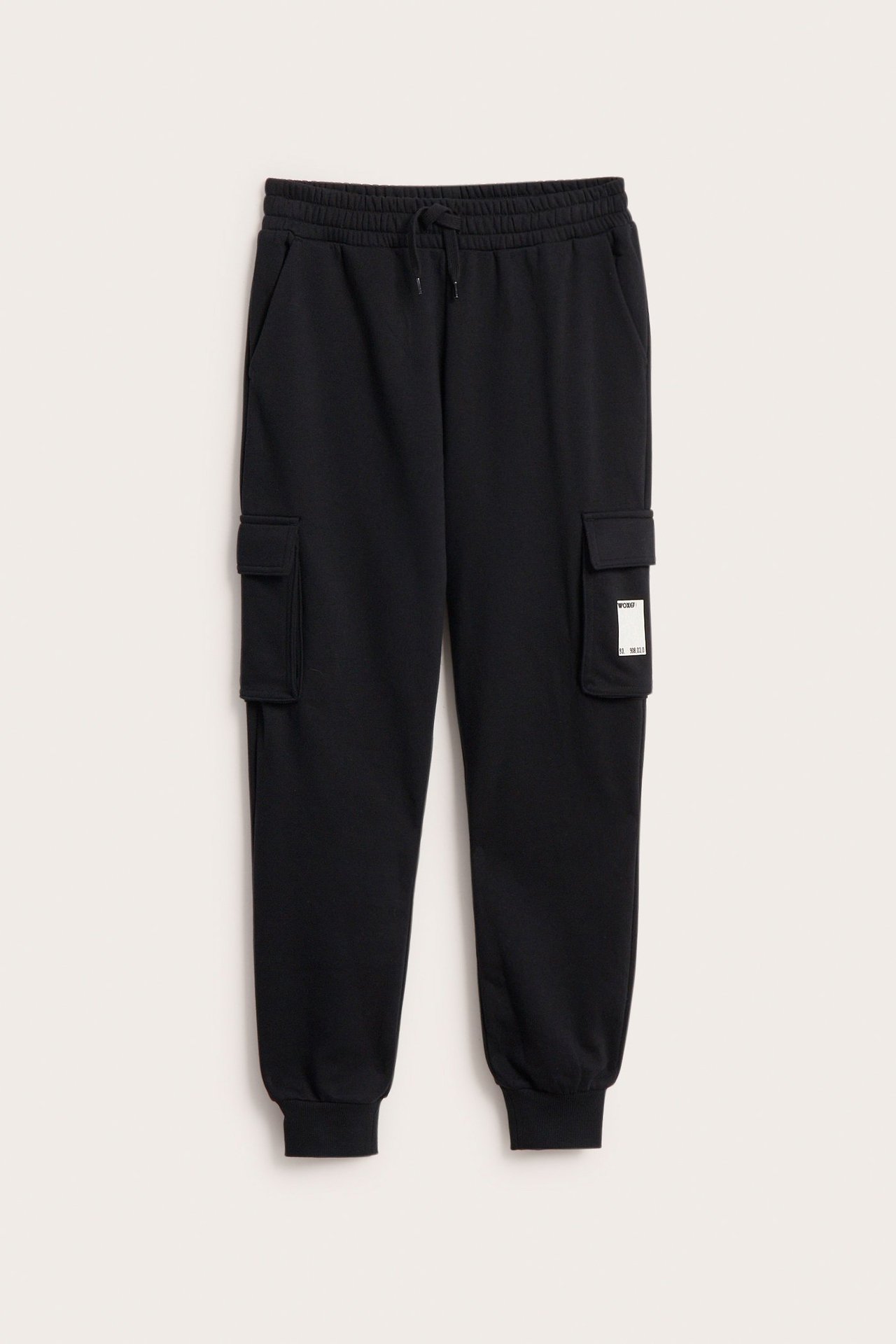 Widok z przodu czarnych spodni dresowych z kieszeniami cargo, ściągaczem i gumowym nadrukiem na jednej nogawce.