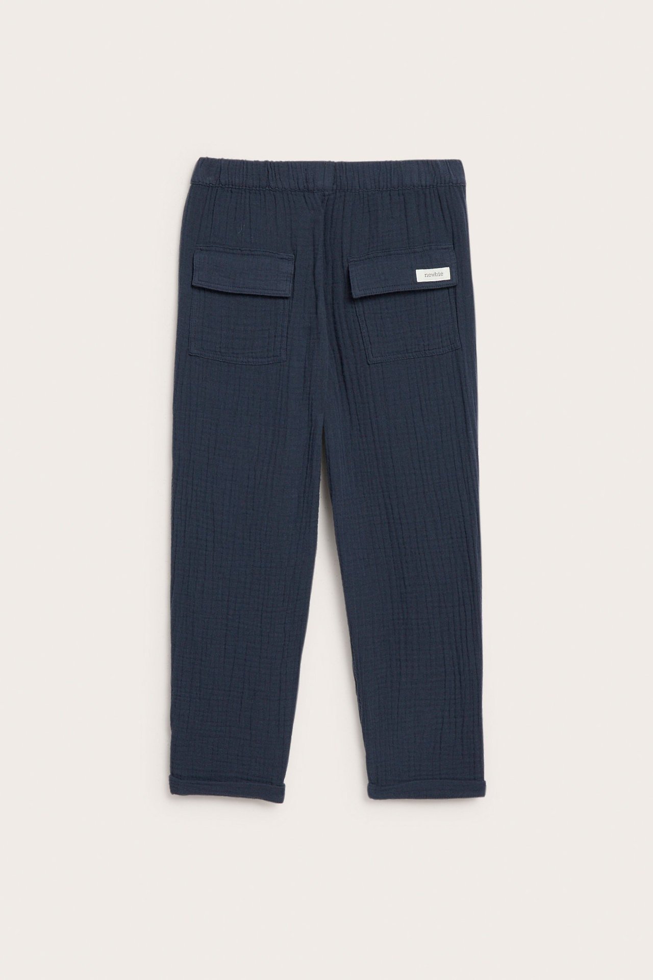 Widok z tyłu: Dziecięce granatowe spodnie z muślinu bawełnianego, z elastycznym pasem, klapowymi kieszeniami i podwiniętymi nogawkami.