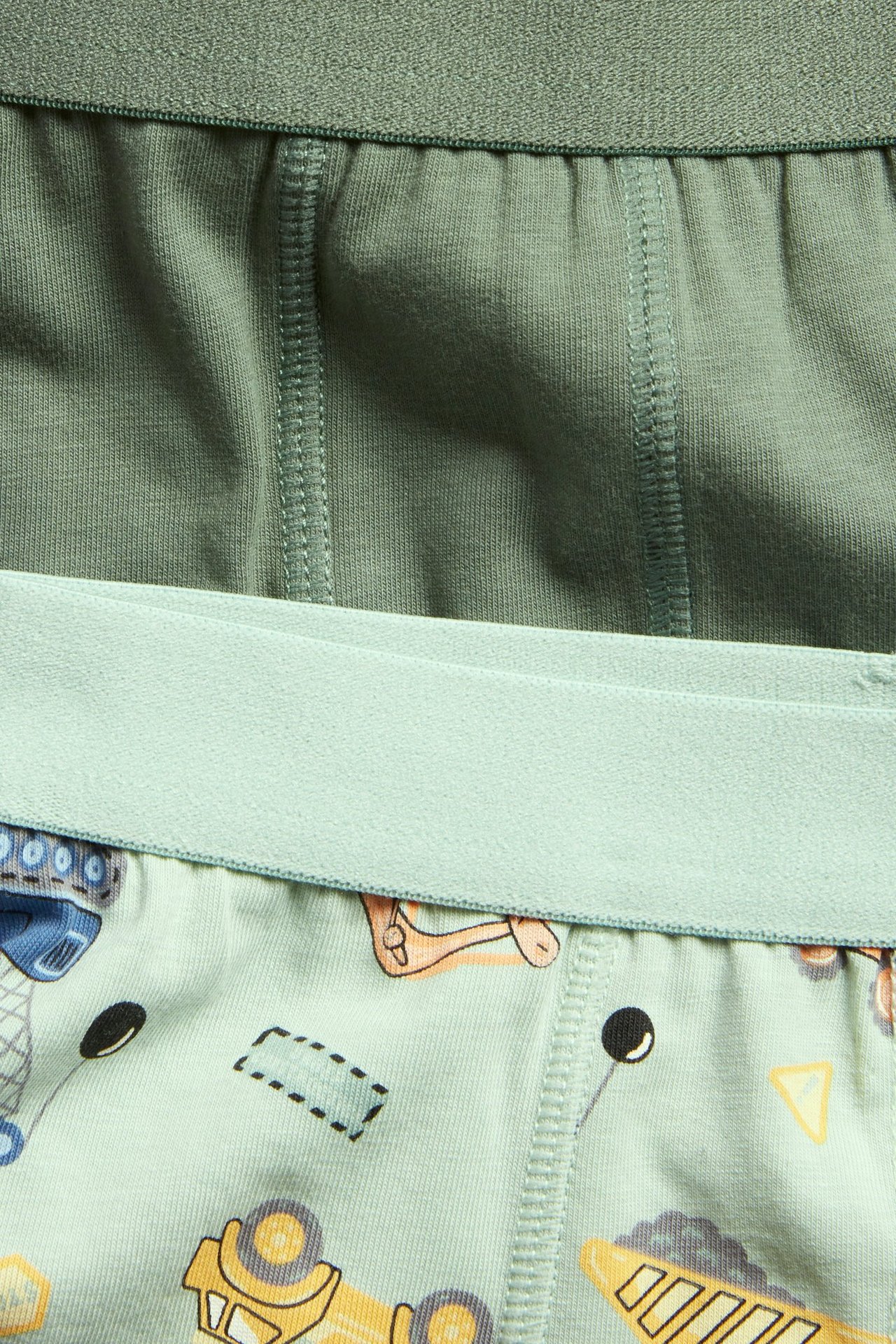 Närbild på barns gröna 2-pack boxerkalsonger: ett par ljust gröna med fordon, ett par enfärgat mörkgröna.