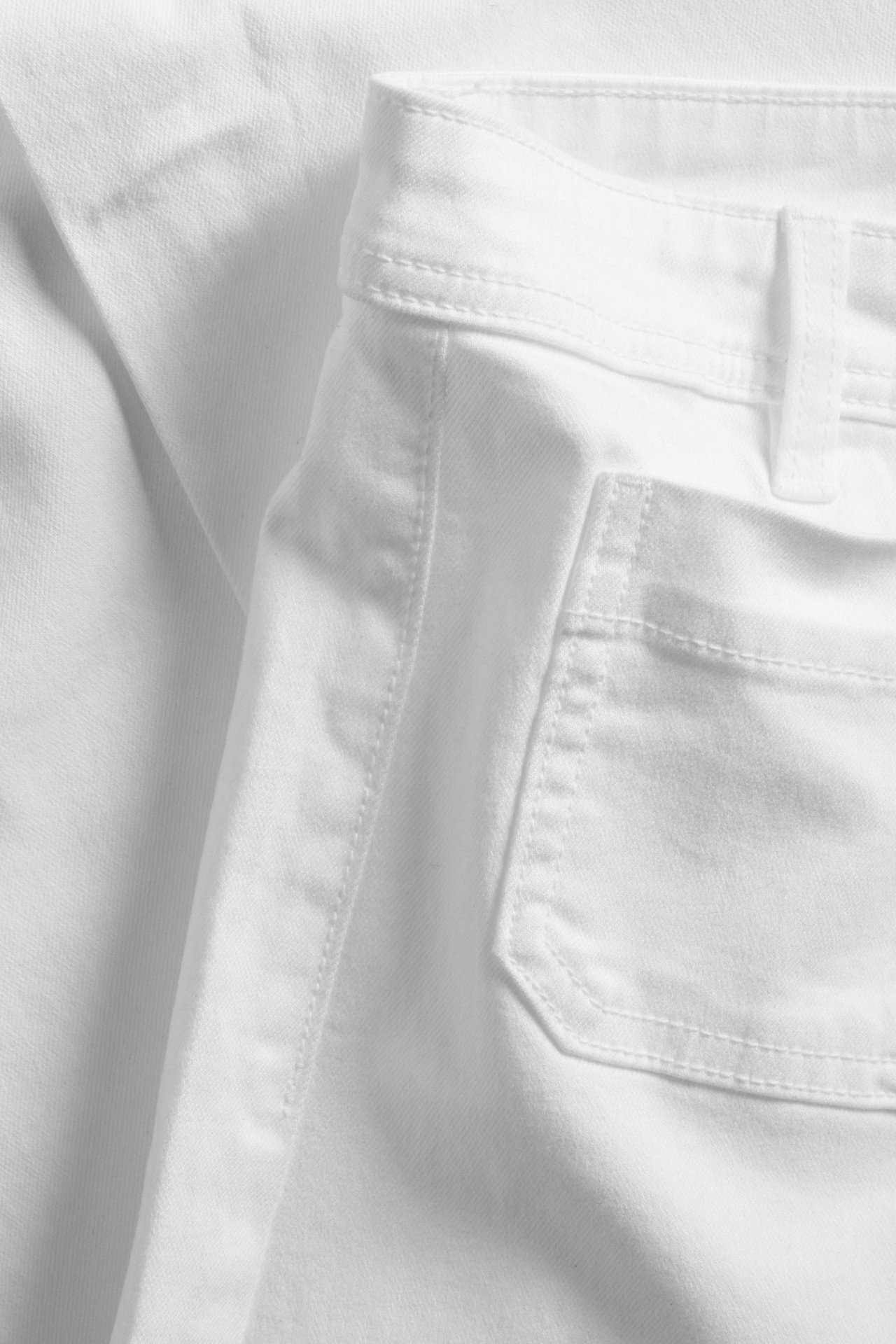 Nærbilde av hvite høye vide jeans med påsydde frontlommer og beltehemper.