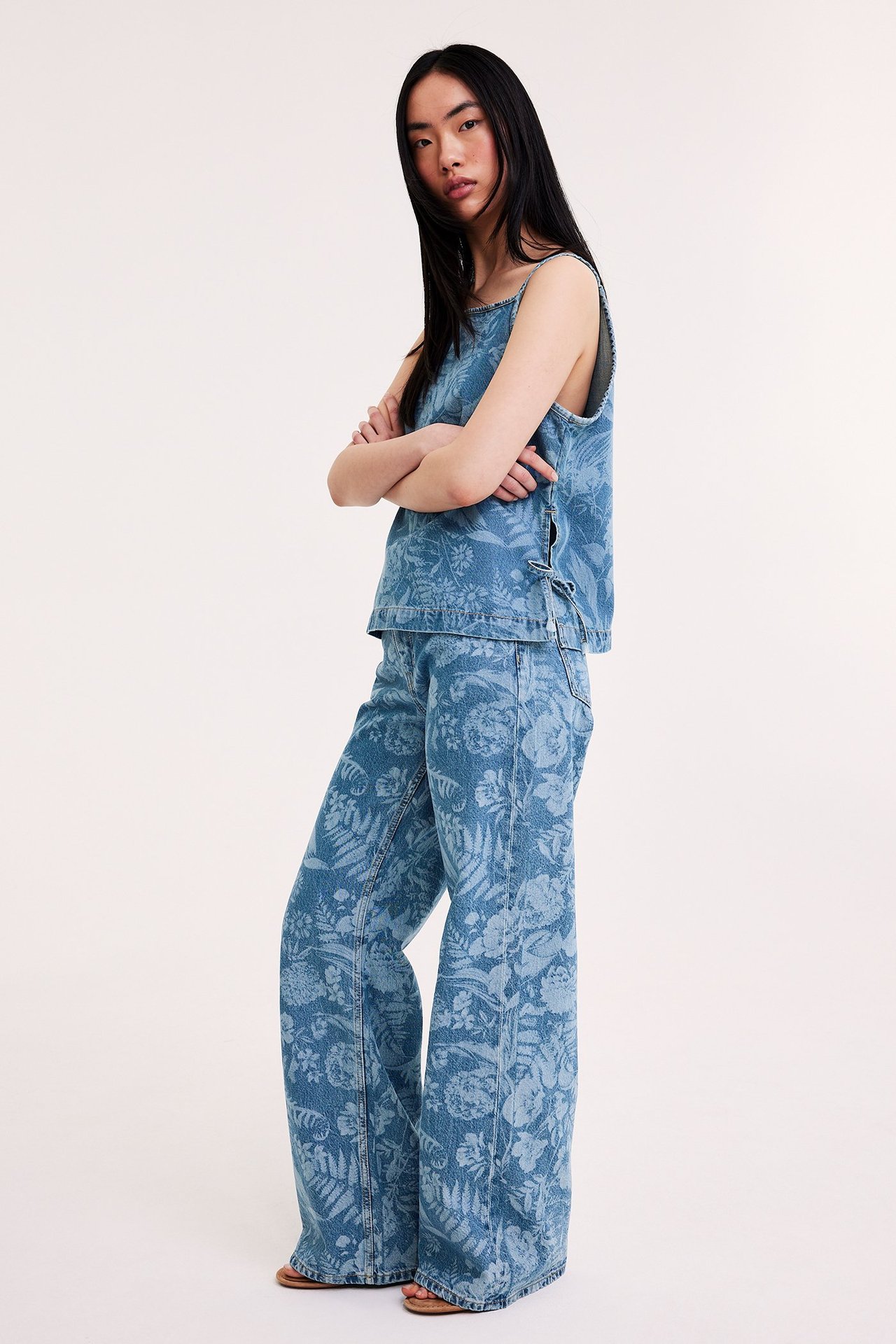 Naisen sivukuva: vaaleansiniset kukkakuvioidut leveälahkeiset farkut ja yhteensopiva hihaton toppi.