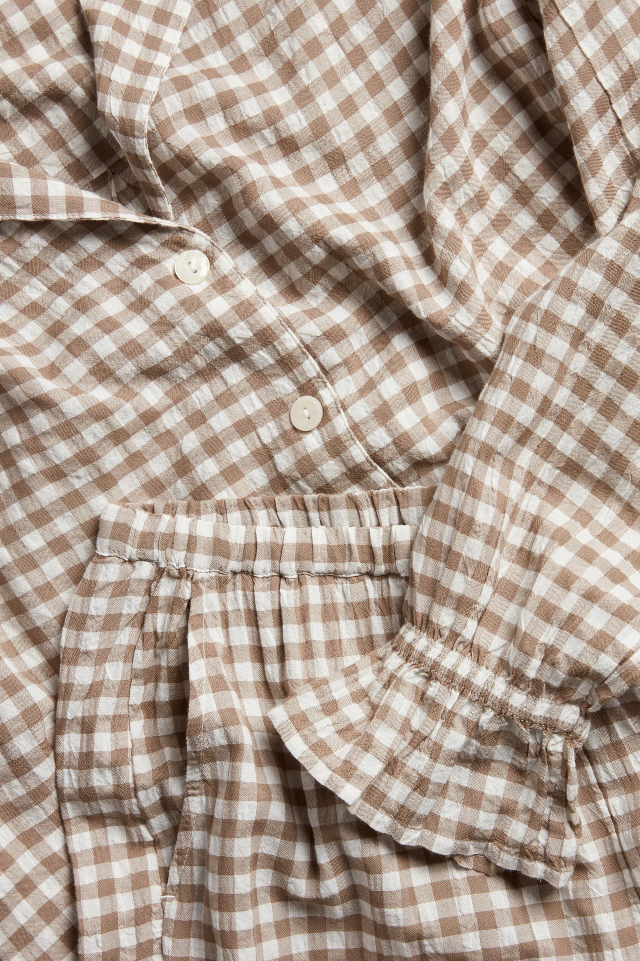 Nærbilde av beige og hvitrutete seersucker-pyjamas med knapper, strikk i midjen og rynkede mansjetter.