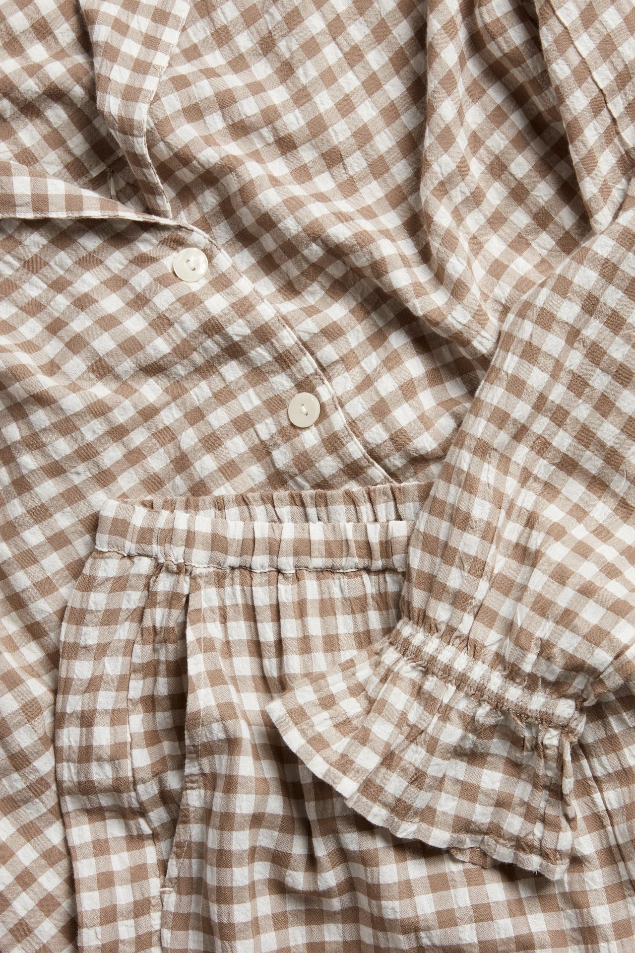 Nærbilde av beige og hvitrutete seersucker-pyjamas med knapper, strikk i midjen og rynkede mansjetter.