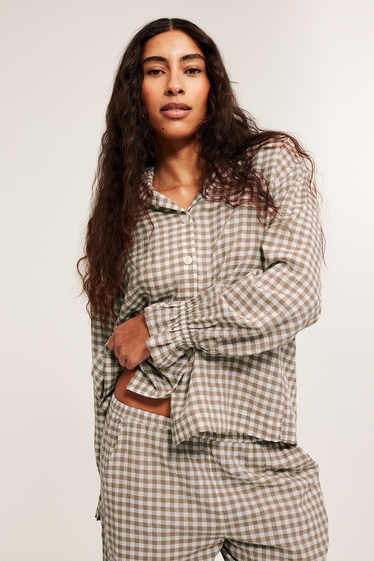 Etunäkymä: Nainen beigessä ruudullisessa seersucker-pyjamassa, jossa napillinen paita ja leveät housut.