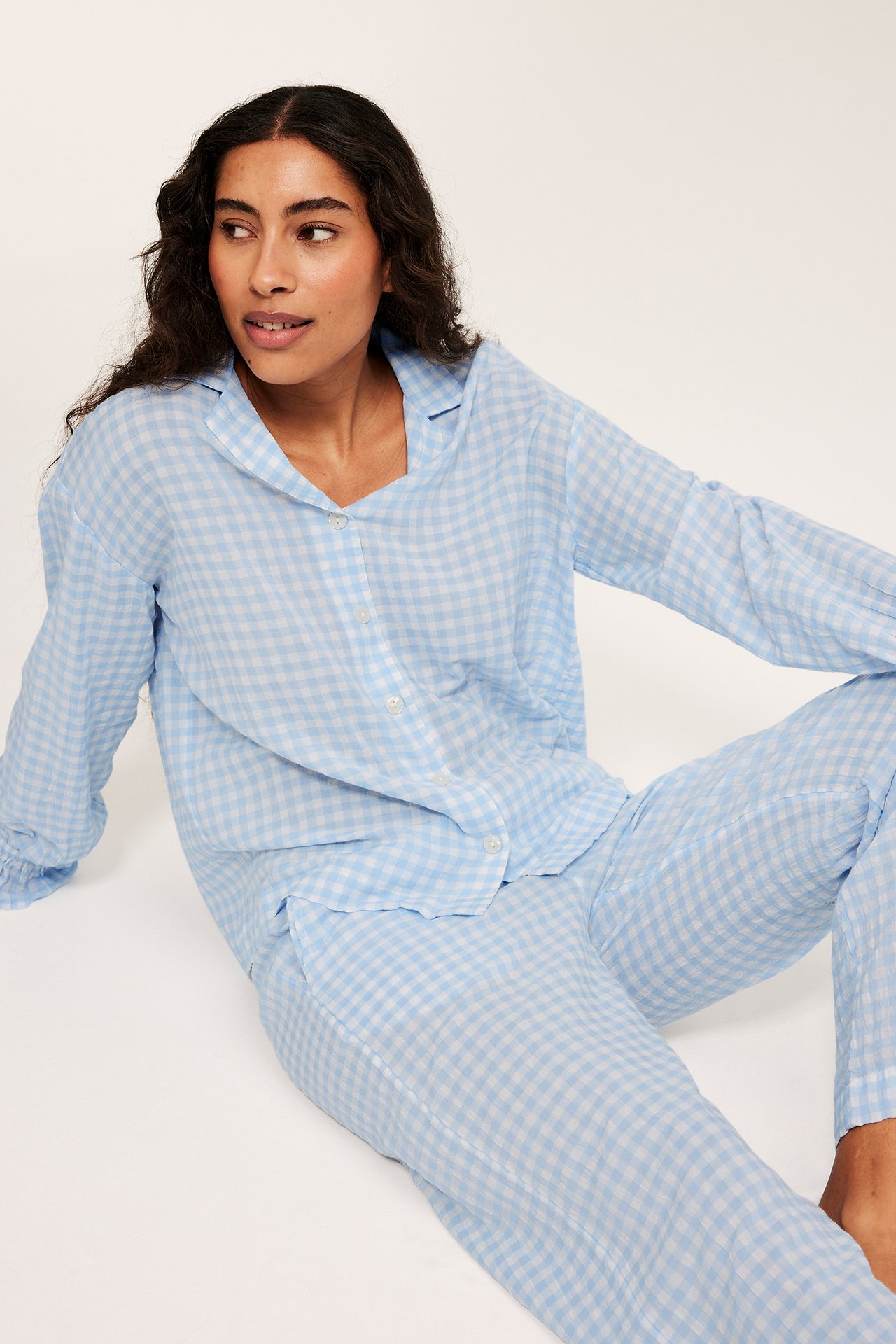Framsidebilde av kvinne i lyseblå rutete seersucker-pyjamas med kneppt topp og bukser.