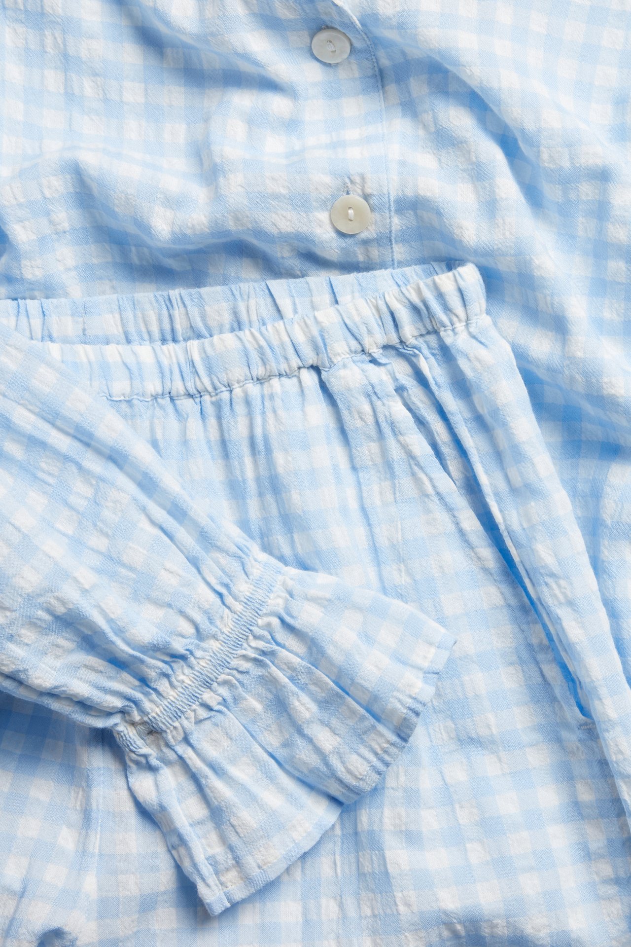 Nærbilde av lyseblå og hvitrutet seersuckerpyjamas med knapper, elastisk midje og rynkede mansjetter.