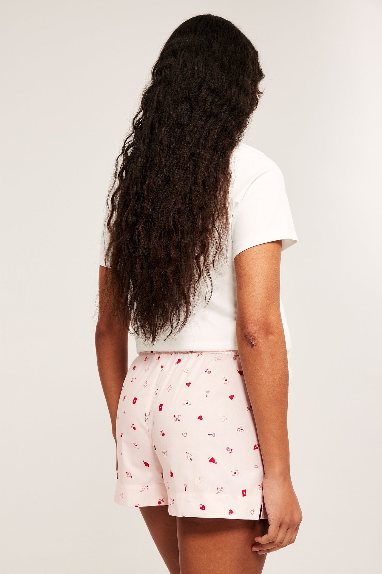 Ryggbilde av kvinne i lyserosa mønstrede pyjamasshorts med hvite knapper og hvit t-skjorte.