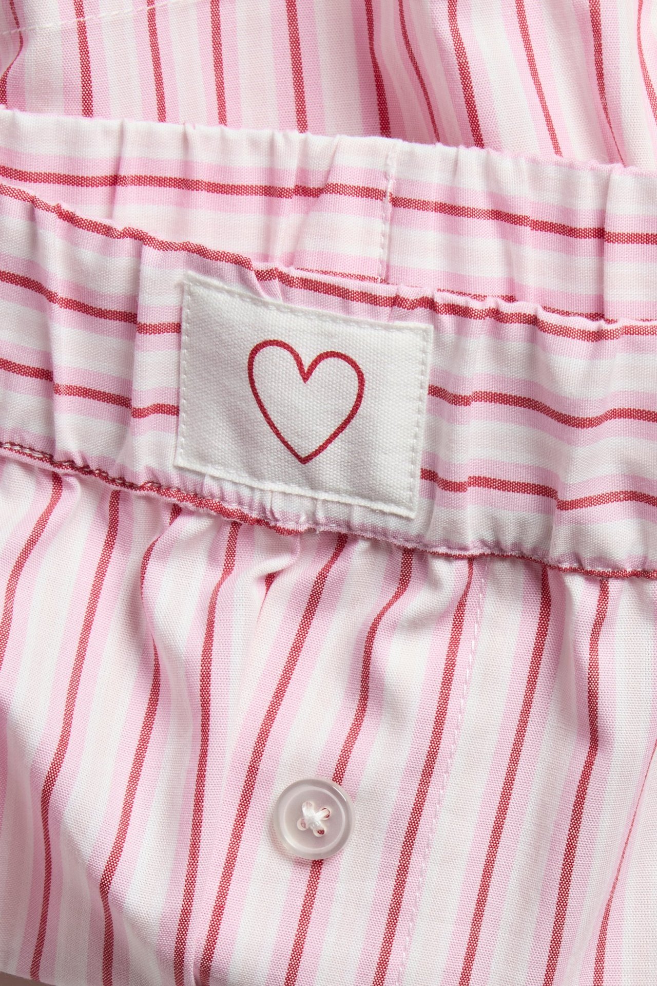 Zbliżenie: Różowe bawełniane szorty piżamowe w paski z elastycznym pasem, sercem i guzikiem.