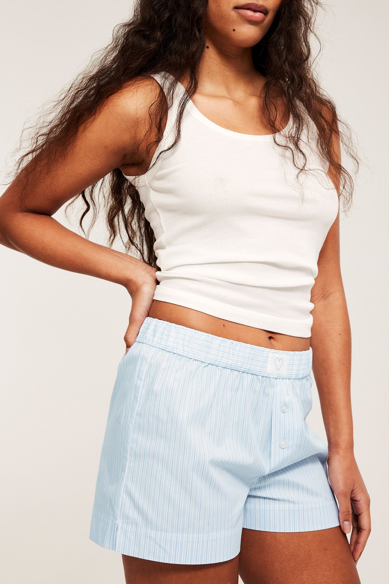 Z przodu: Kobieta w niebieskich, pasiastych szortach piżamowych z bawełny, z gumką, guzikami i białym topem.