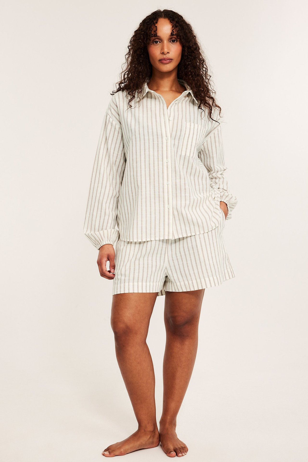 Widok z przodu kobiety w beżowej piżamie w paski, koszuli i pasujących szortach.