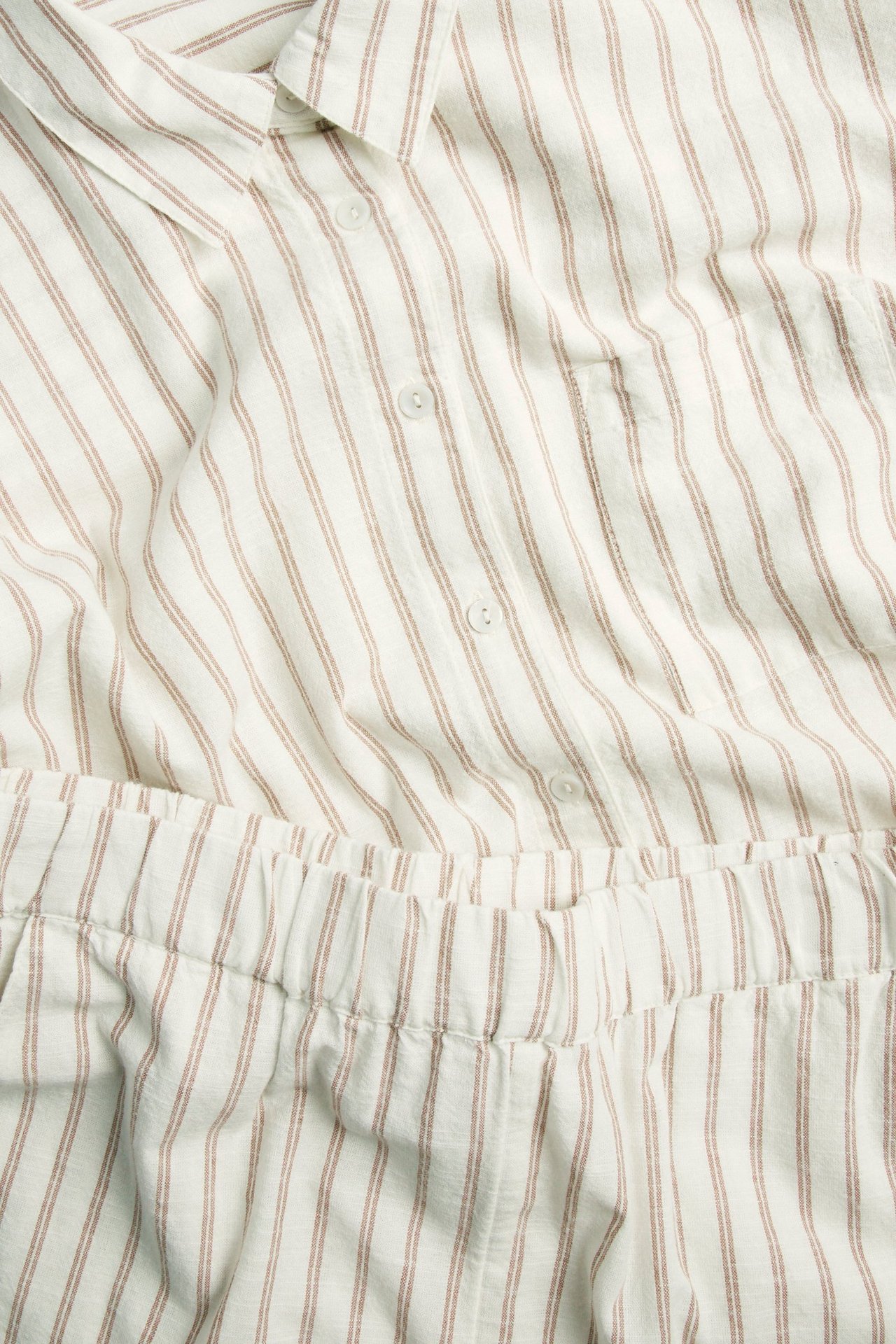 Närbild av beige randig pyjamas i bomull: skjorta med knappar och ficka, samt shorts med resårmidja.