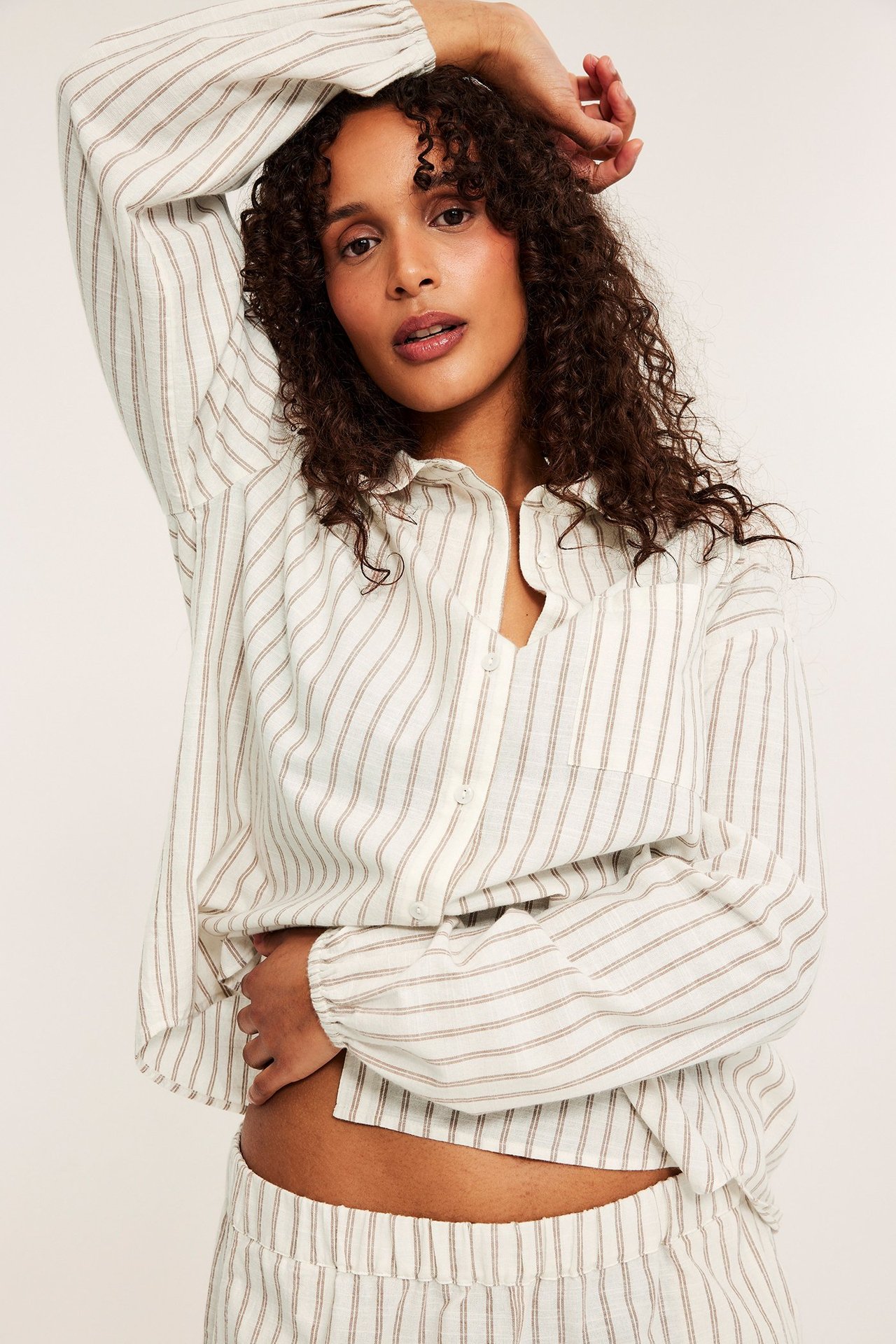 Widok z przodu: Kobieta w beżowym bawełnianym zestawie piżamowym w paski z koszulą i szortami.