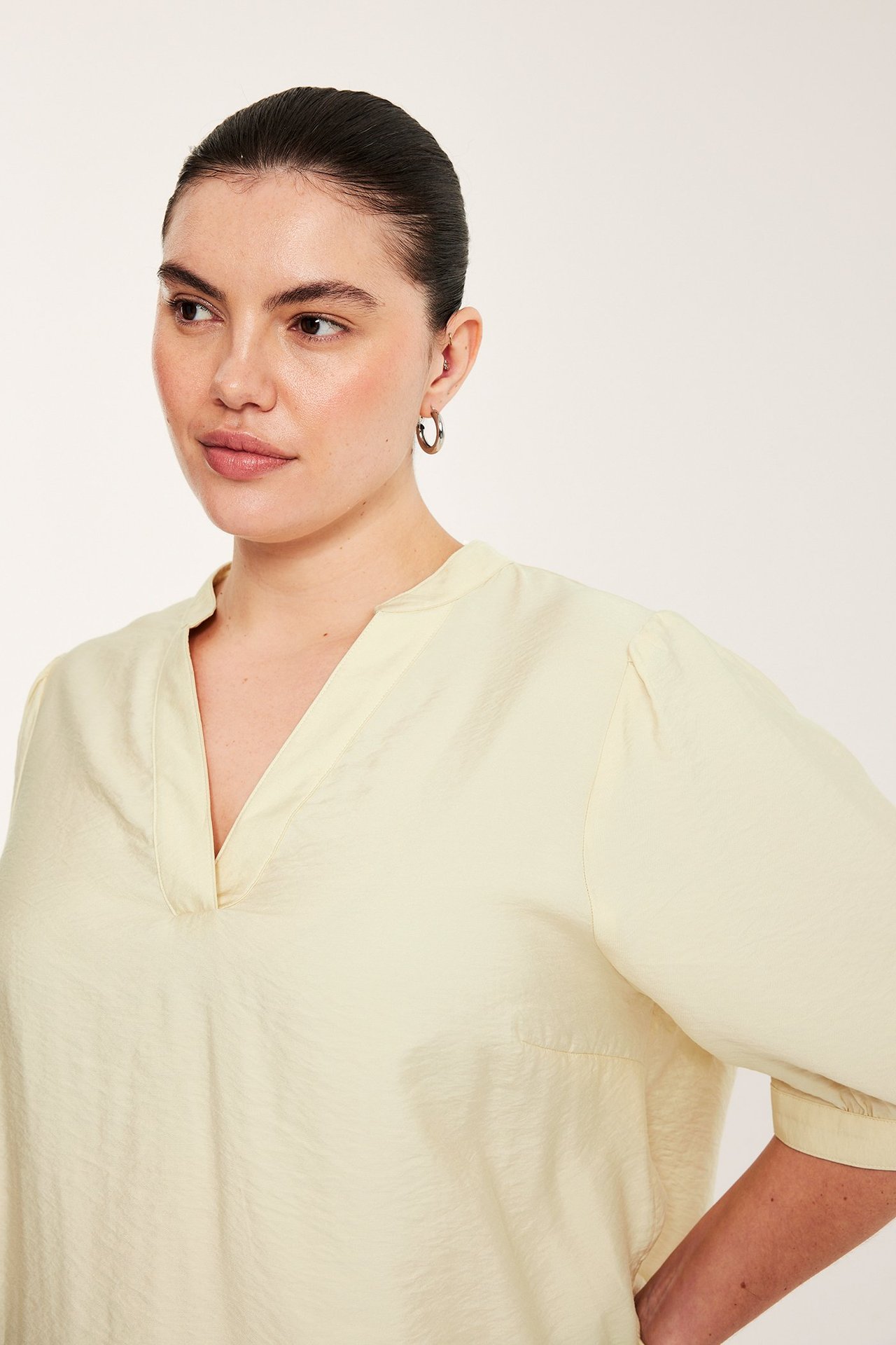 Kobieta nosi jasnożółtą bluzkę pop-over z dekoltem V, rękawami 3/4 i srebrne kolczyki.