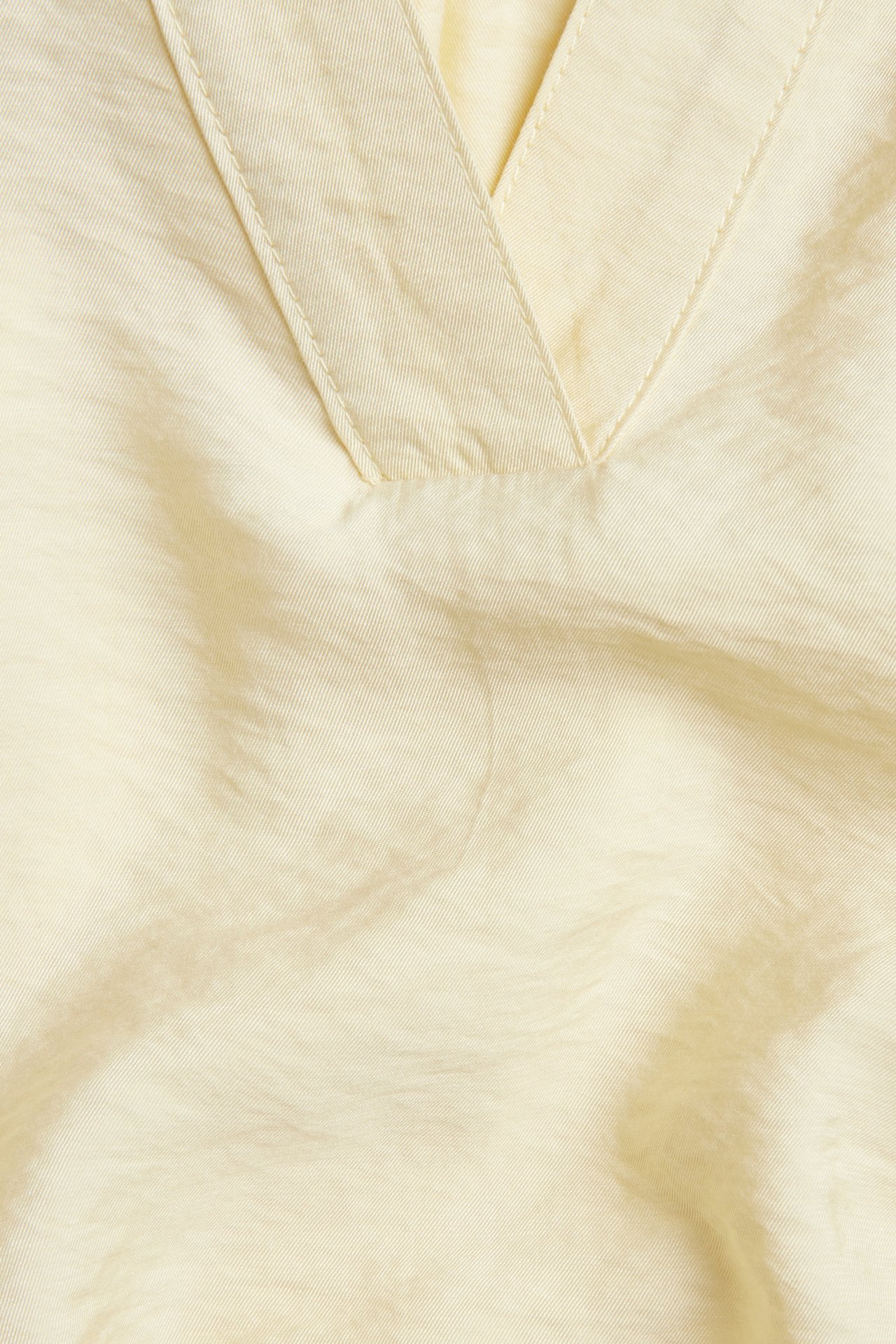 Nærbilde av en lys gul V-hals bluse, laget av et mykt, teksturert viskoseblandingsstoff.