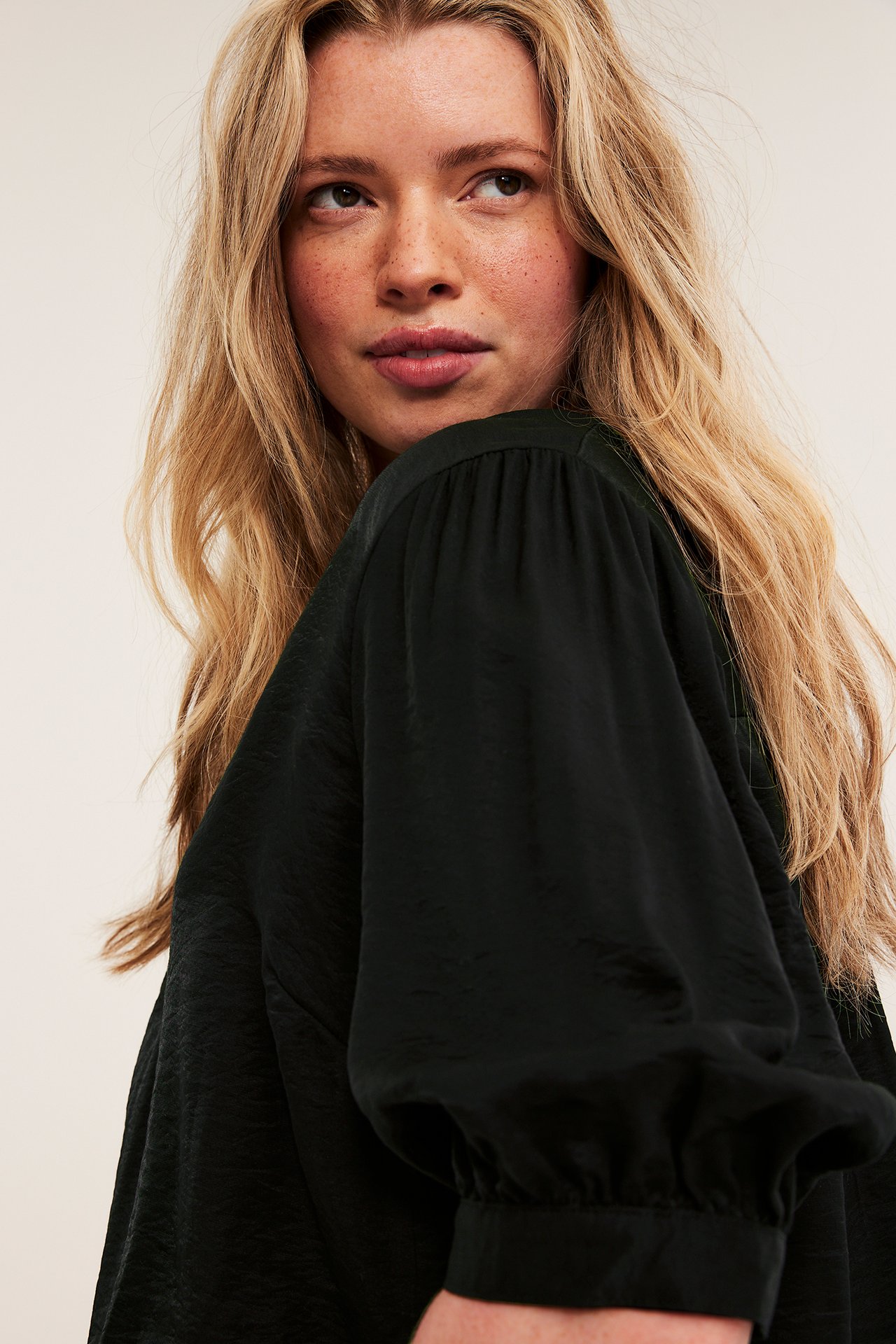Närbild av en kvinna i en svart blus med diskret struktur och voluminösa puffärmar.